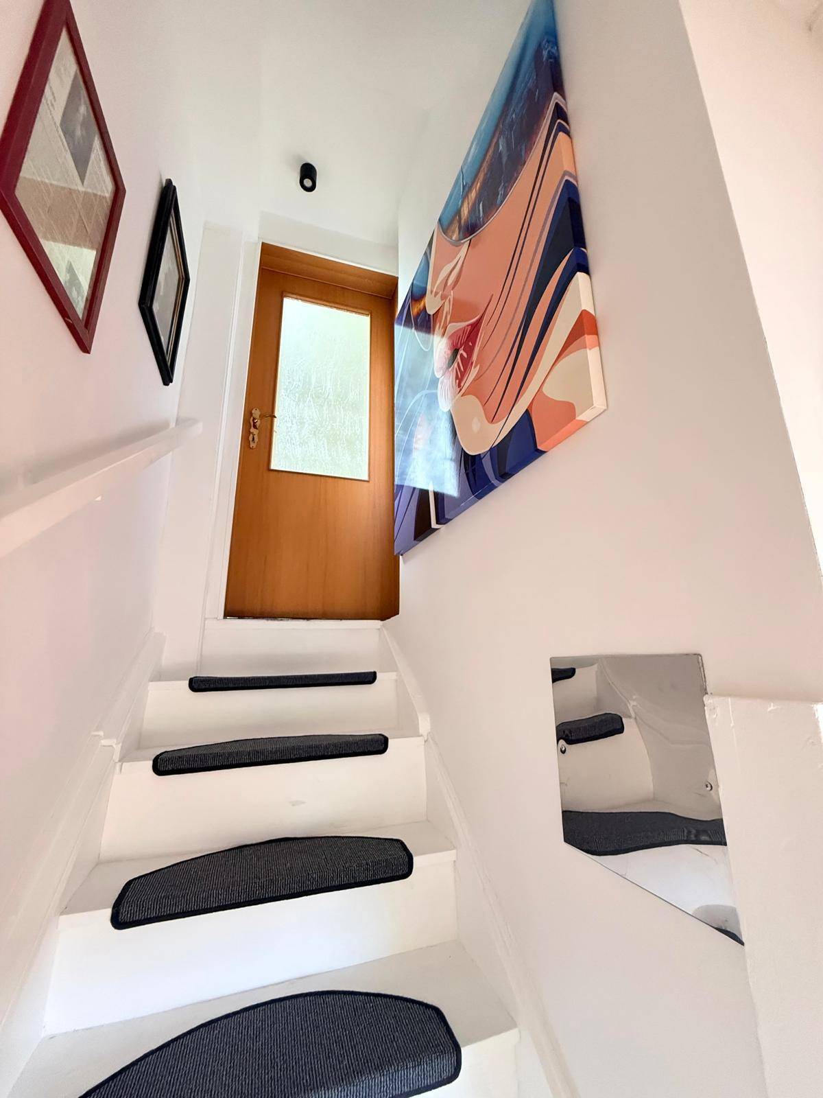 Weißer Treppenaufgang mit dunklen Stufenmatten und modernem Kunstwerk an der Wand.