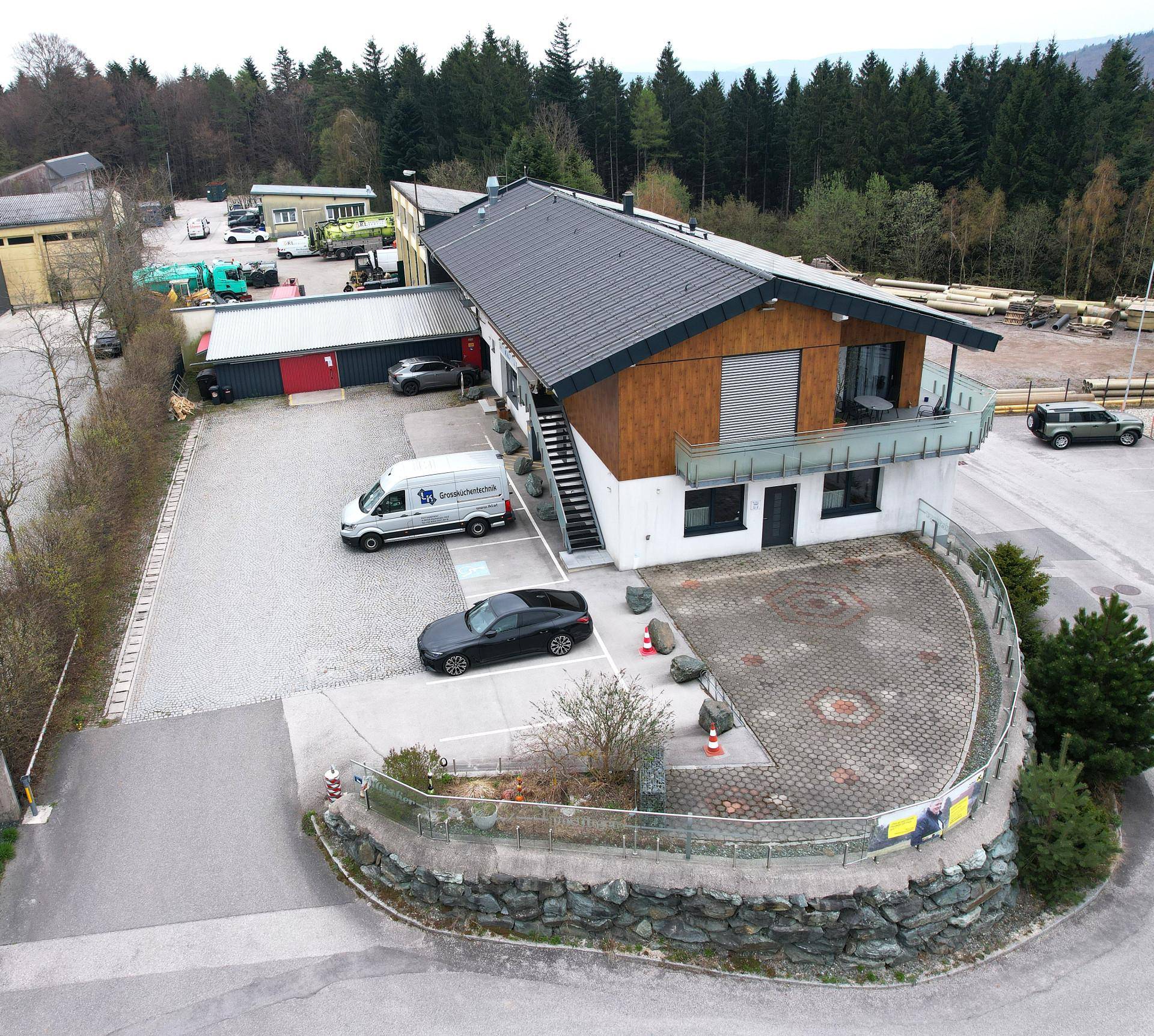 Luftaufnahme eines modernen Gebäudes mit Holzfassade, umgeben von Wald und weitläufigen Parkplätzen.