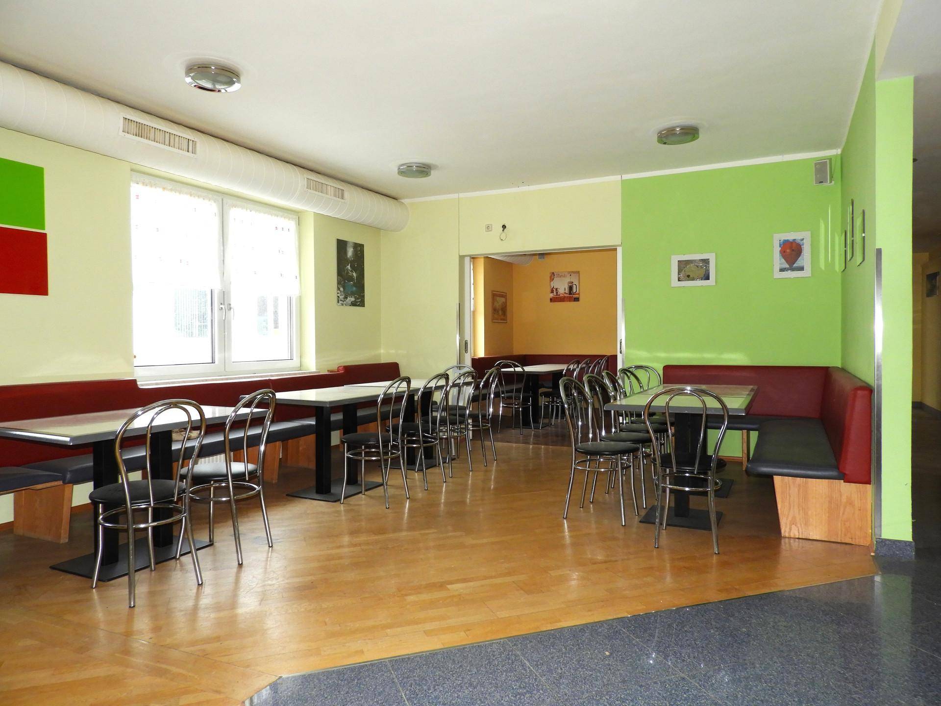 Geräumiger Speisesaal mit Holzboden, langen Tischen und Sitzbänken in lebhaften Farben, hell beleuchtet.