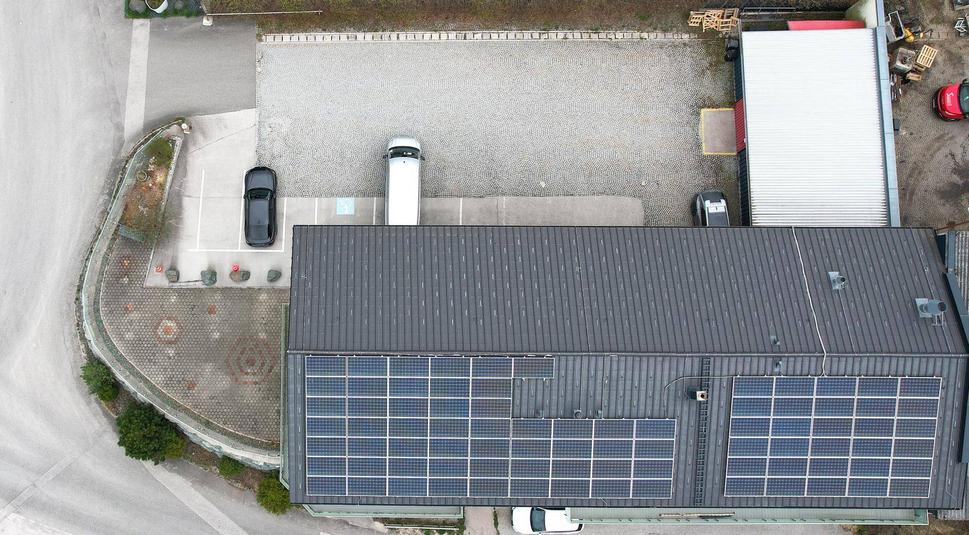 Dachansicht eines Gebäudes mit Photovoltaikanlage und umliegenden Parkflächen, von oben betrachtet.