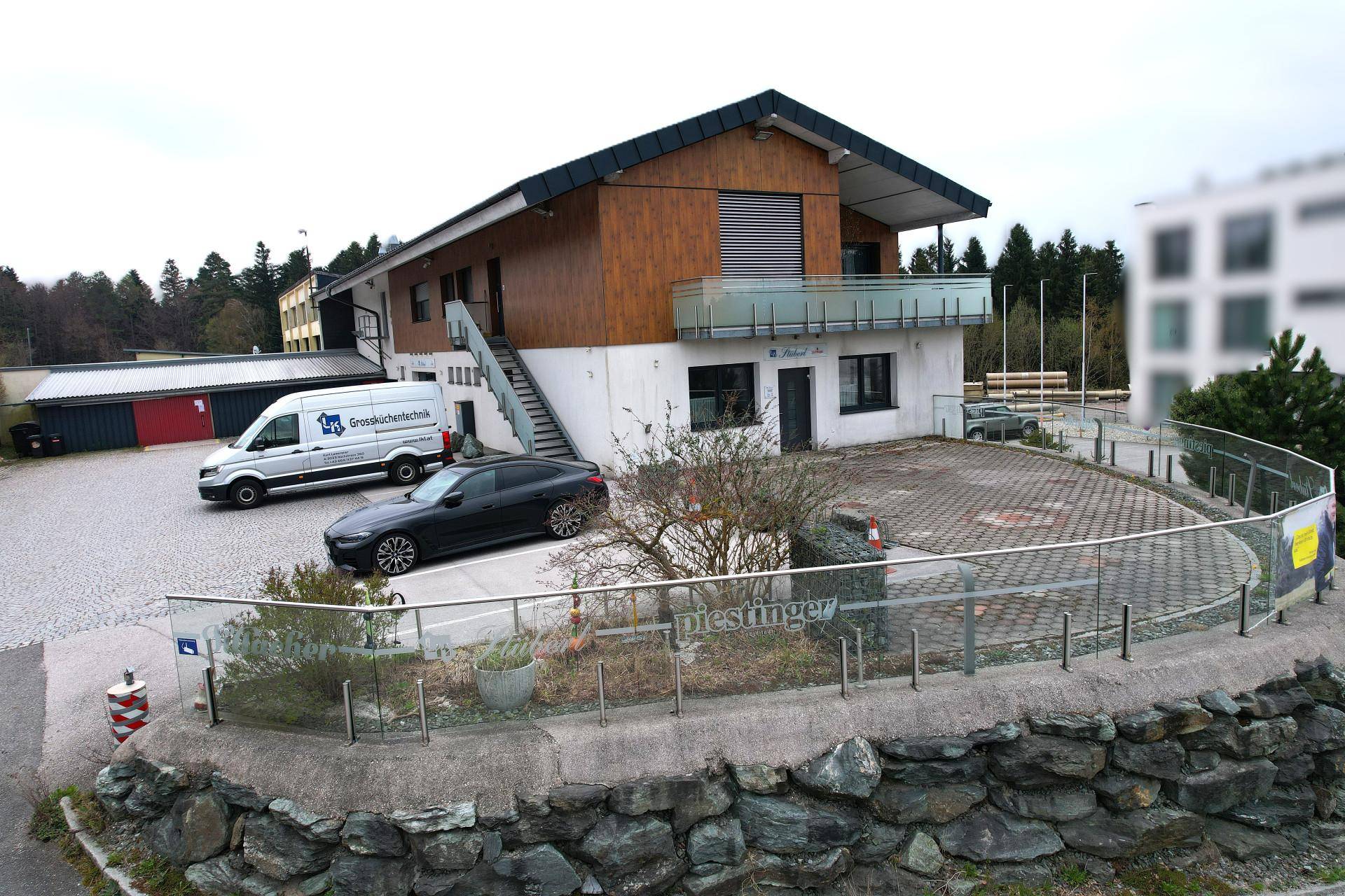 Modernes Gebäude mit Holzfassade, Balkon und großem Parkplatzbereich, funktional und ansprechend.