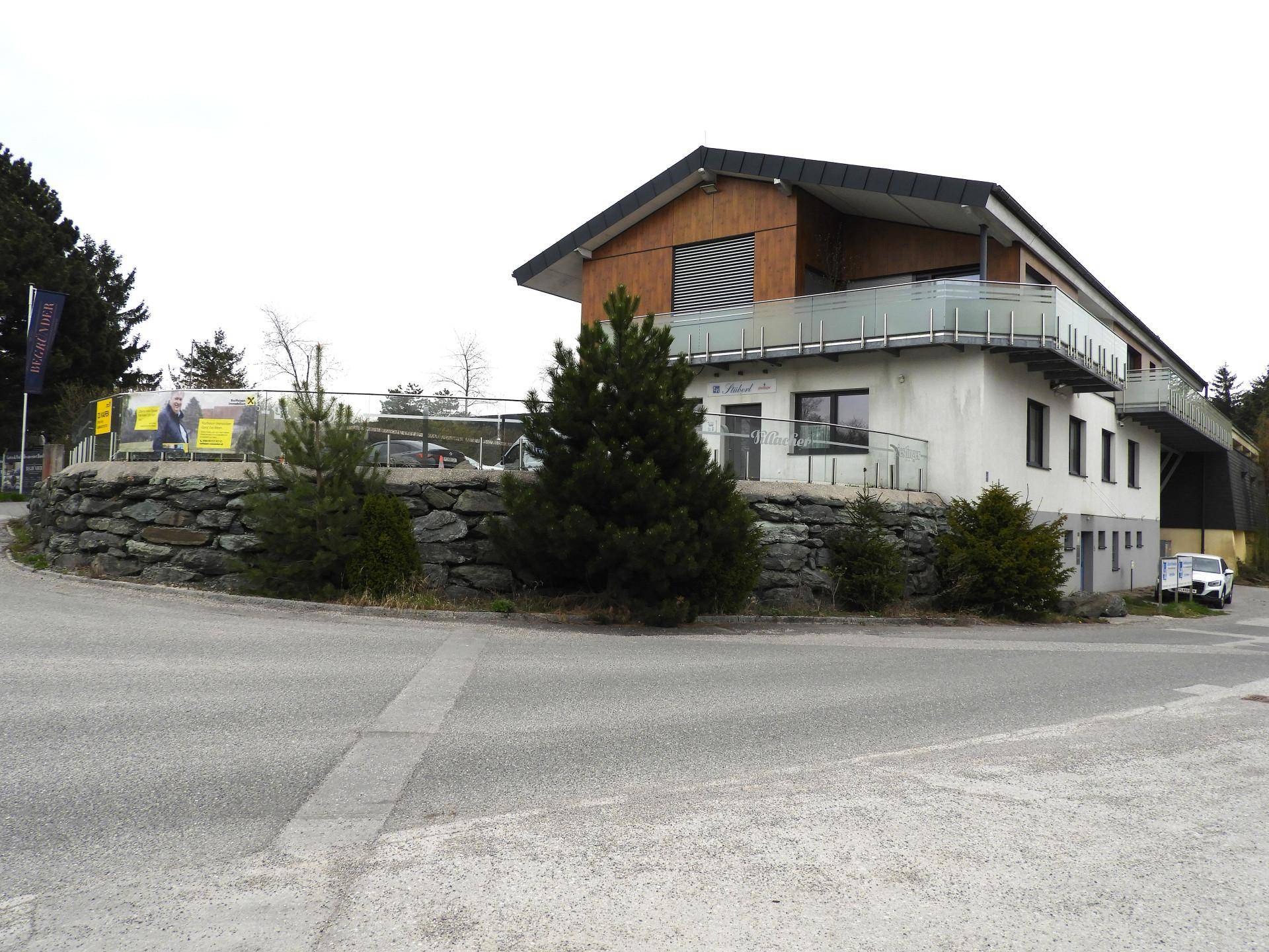 Modernes Gebäude mit Holzfassade, Balkon und Steinfundament, eingebettet in die Landschaft.