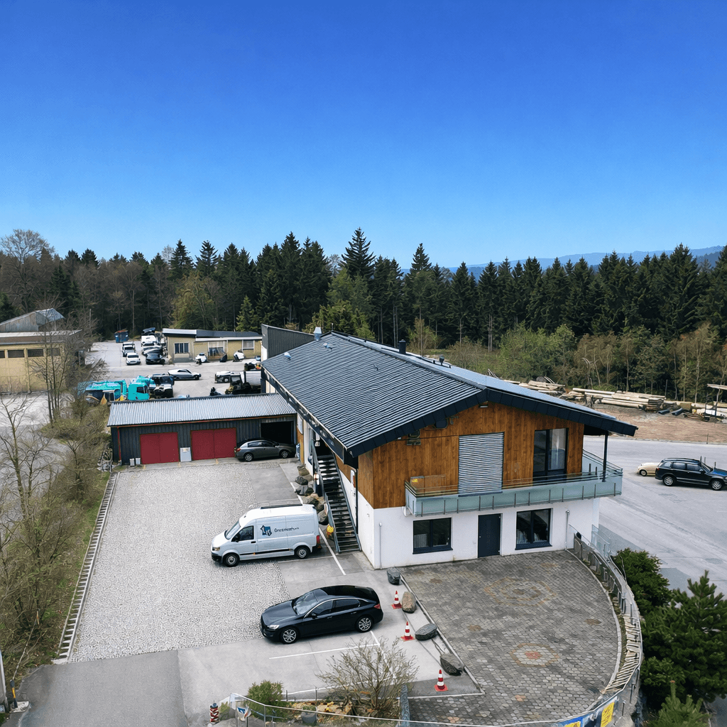 Luftaufnahme eines modernen Gebäudes mit Holzfassade, umgeben von Wald und weitläufigen Parkplätzen.