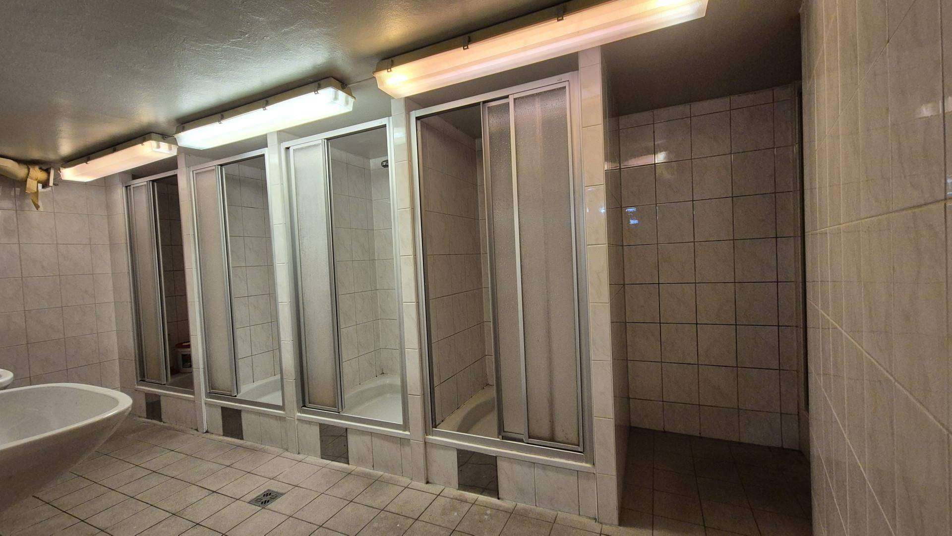 Gemeinschaftsduschbereich mit mehreren Duschkabinen und Fliesenboden.