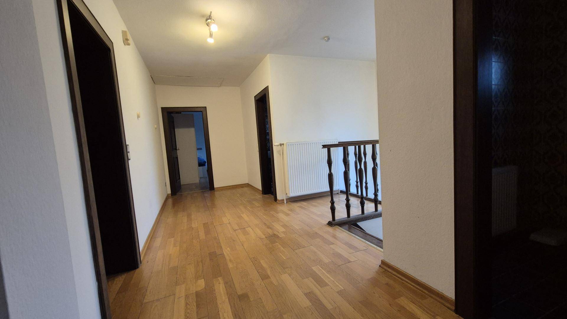 Flur im Obergeschoss mit Holzboden und Geländer, der zu mehreren Zimmern führt.