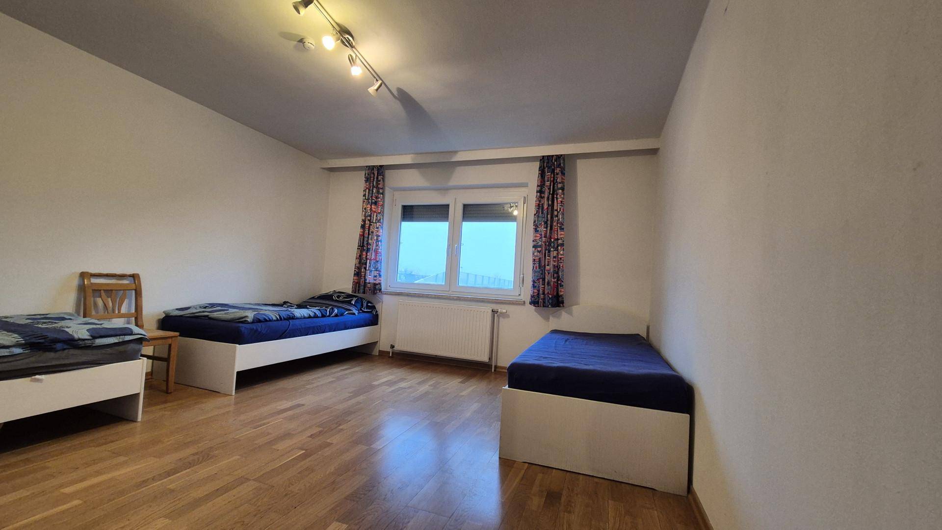 Schlafzimmer mit drei Einzelbetten, Holzboden und Fenster mit Blick nach draußen.