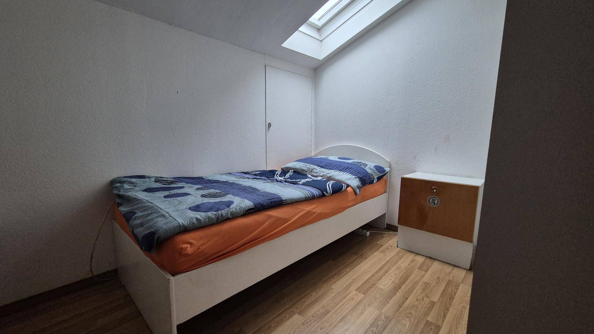 Dachgeschoss-Schlafzimmer mit Einzelbett, Holzboden und einem Dachfenster für natürliches Licht.