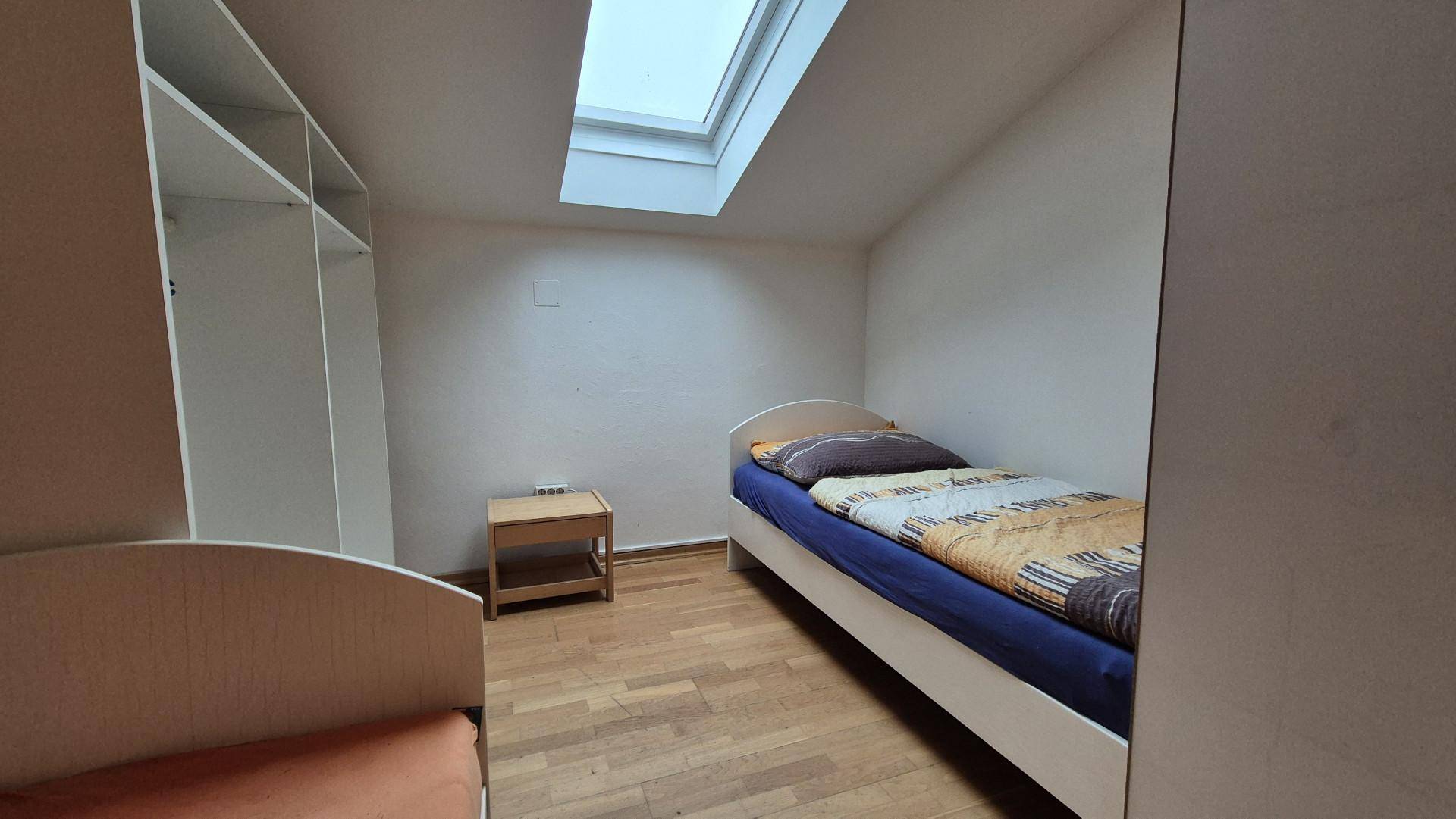 Dachgeschoss-Schlafzimmer mit Einzelbett, Holzboden und einem Dachfenster.