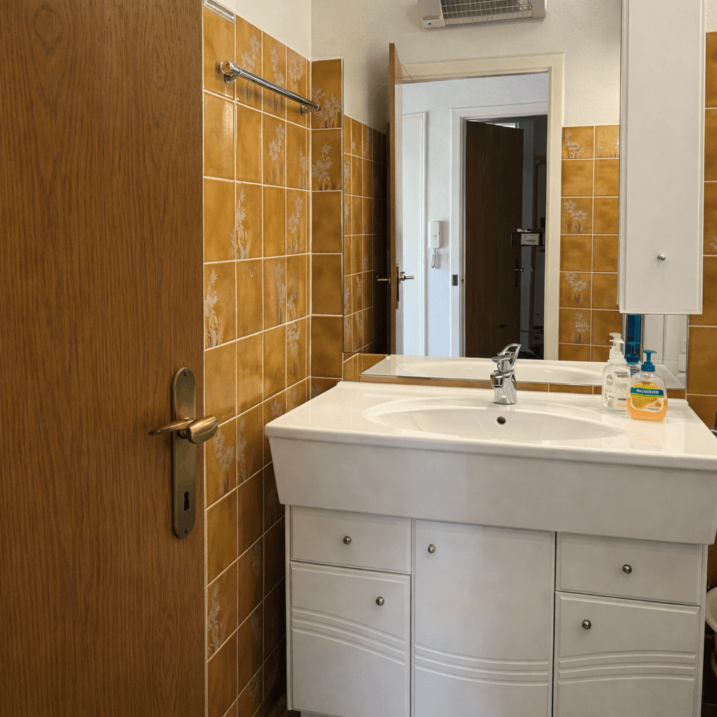Badezimmer mit Waschbecken, Spiegelschrank und braunen Fliesen im Retro-Stil.