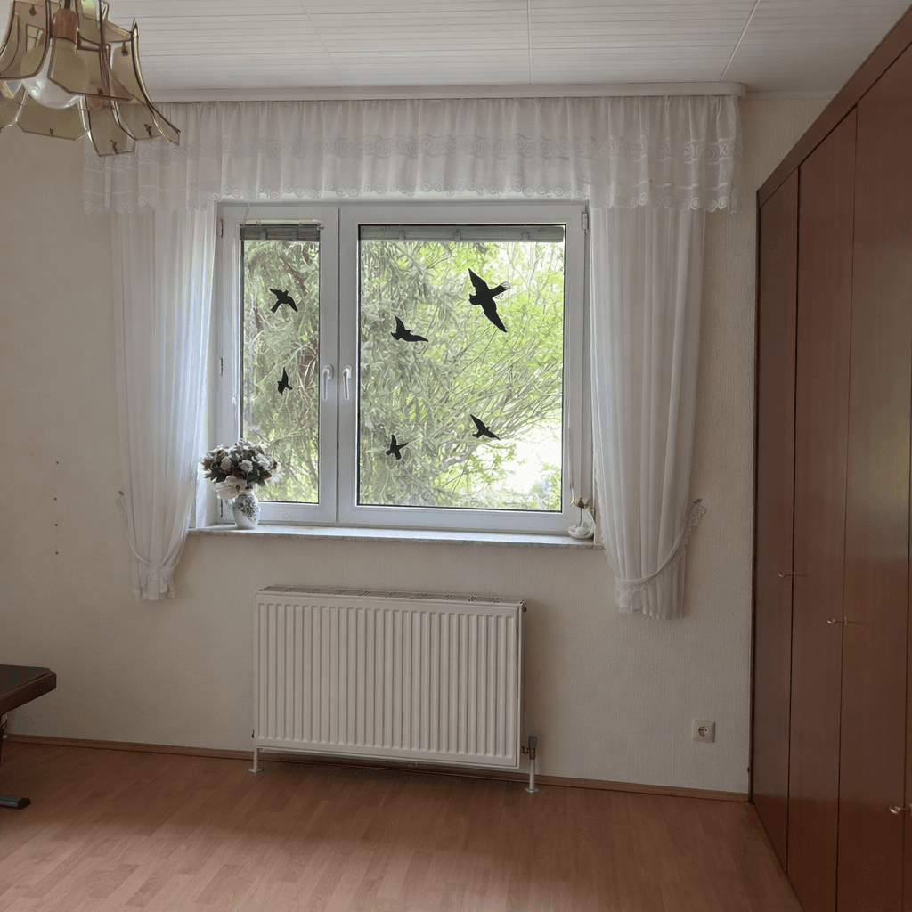 Helles Wohnzimmer mit Parkettboden, großem Fenster und Blick ins Grüne.