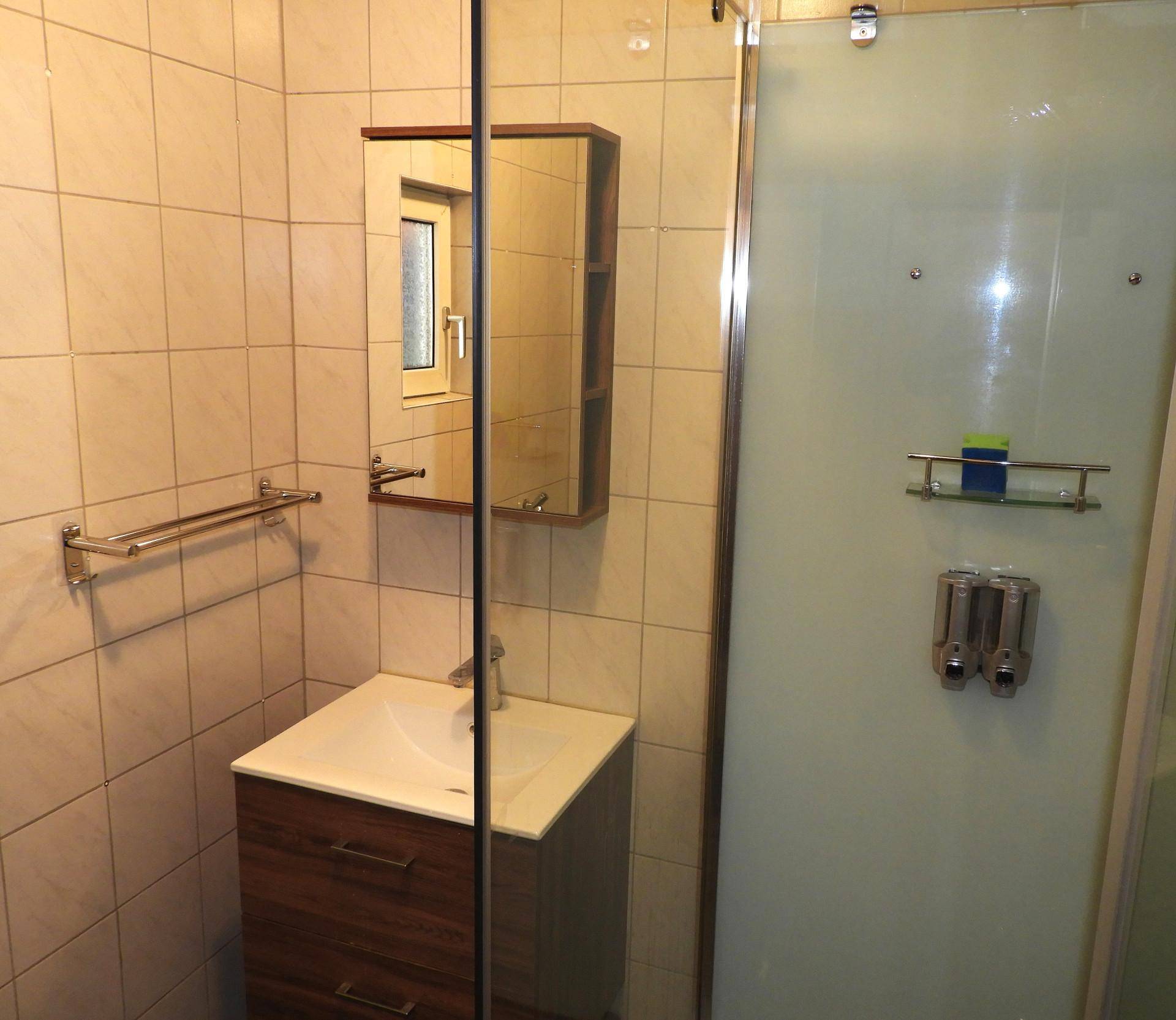 Badezimmer mit Duschkabine, Waschbeckenunterschrank und Spiegelschrank.