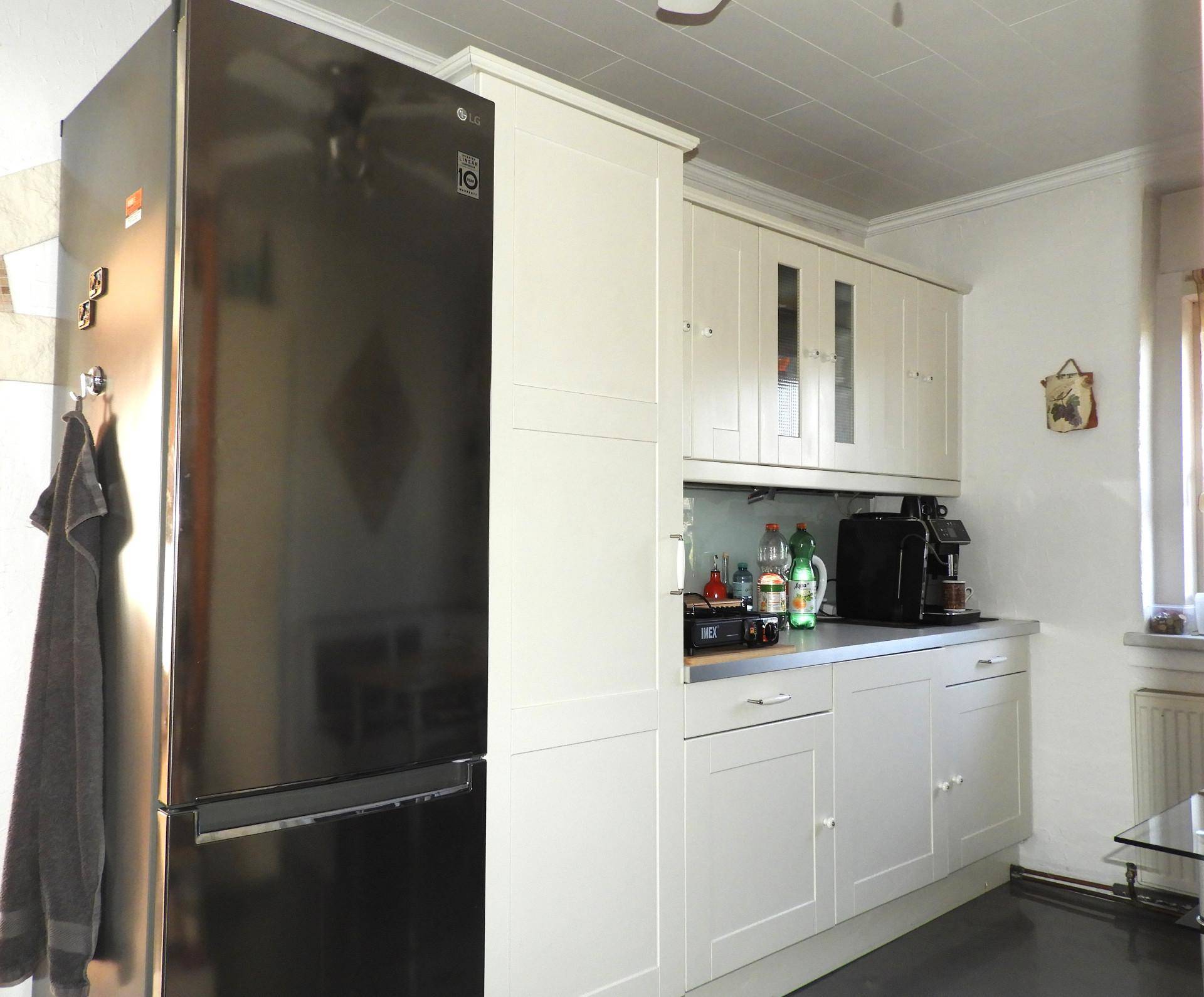 Küche mit weißen Schränken, schwarzem Kühlschrank und Kaffeemaschine.