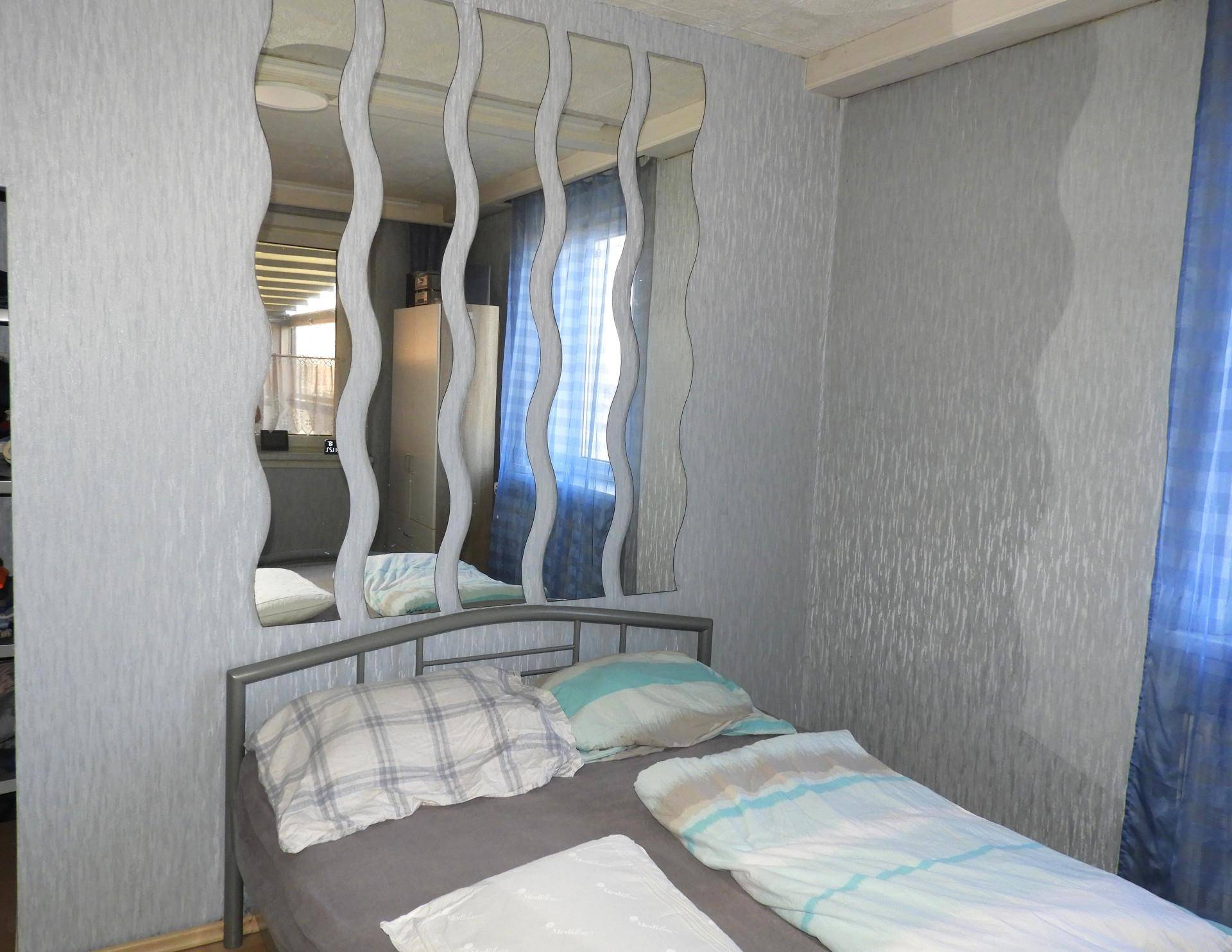 Schlafzimmer mit Doppelbett, grauer Tapete und dekorativen Spiegeln.