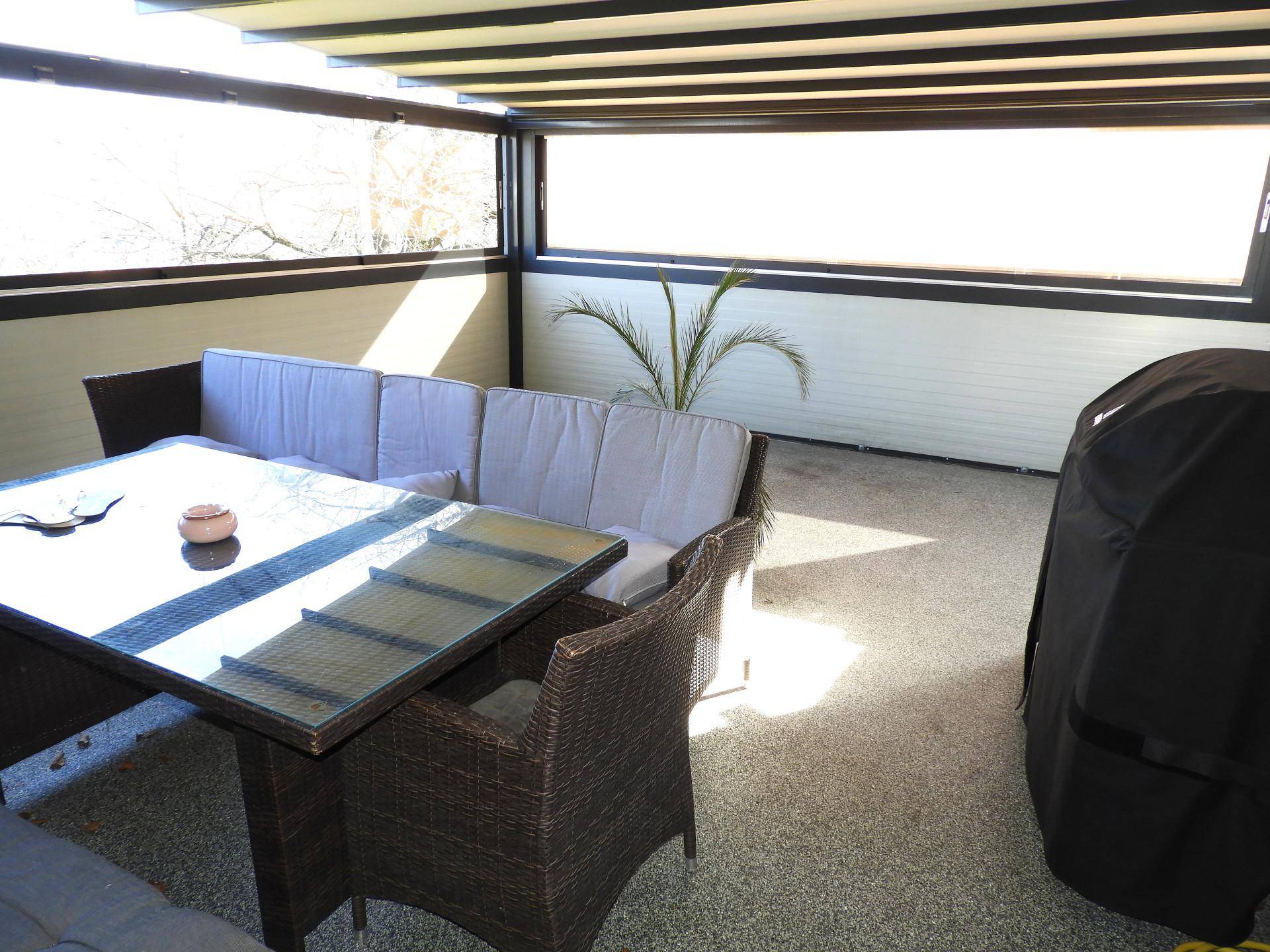 Überdachte Terrasse mit Rattanmöbeln, Esstisch und Pflanzen.