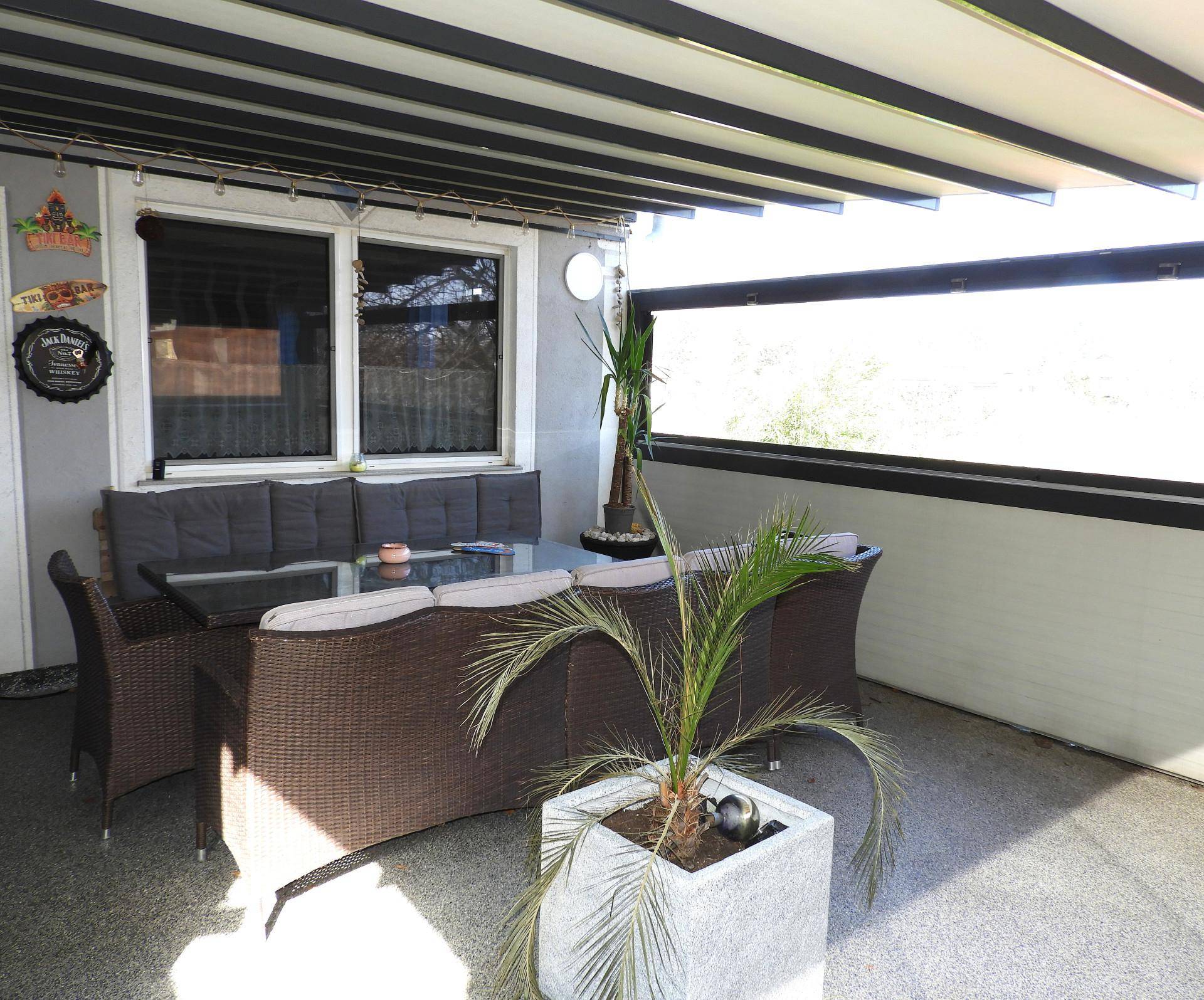 Sonnige Terrasse mit bequemen Sitzgelegenheiten und einer Palme in einem Topf.