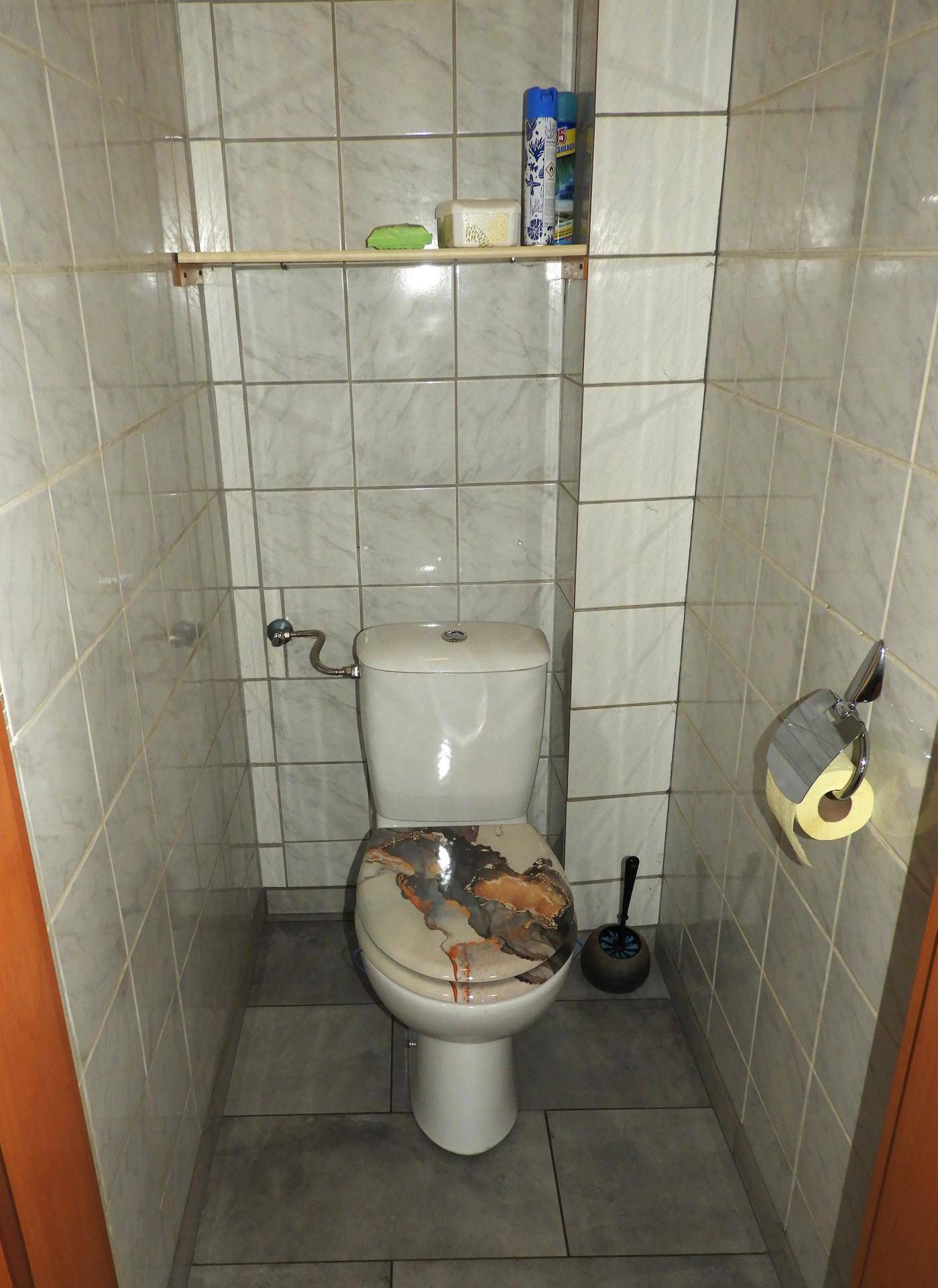 Gäste-WC mit gefliesten Wänden und einem Stand-WC mit gemustertem Deckel.
