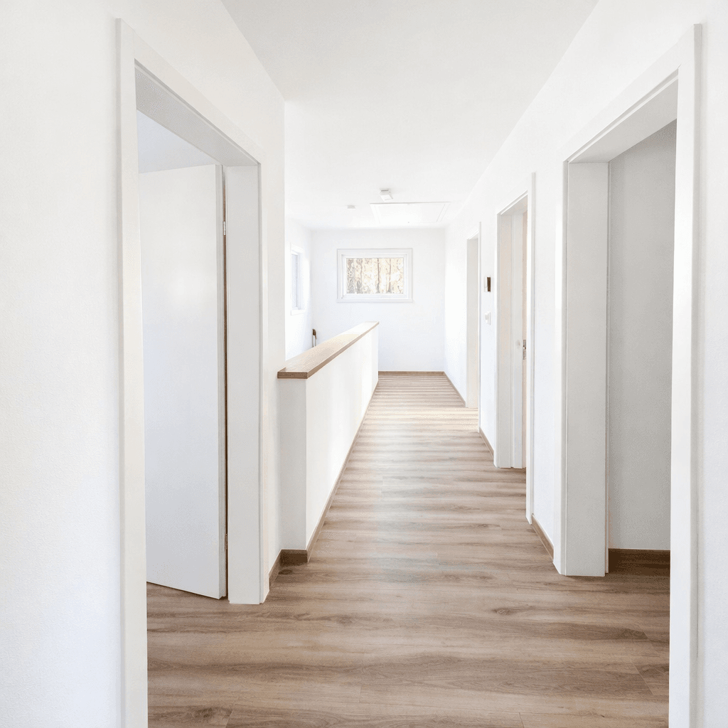 Heller Flur mit Laminatboden, weißen Wänden und einem Fenster am Ende, das Tageslicht hereinlässt.