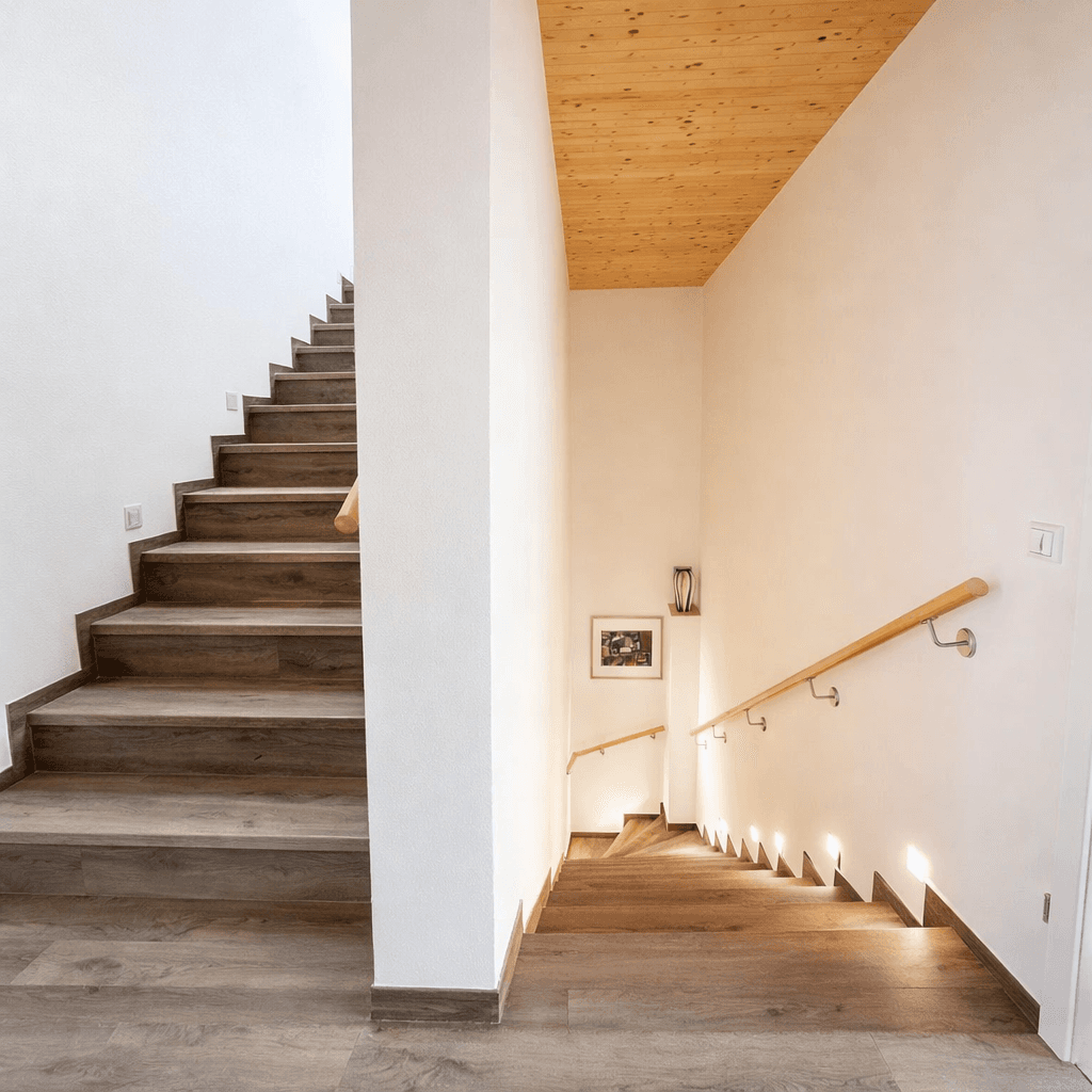 Moderne Holztreppe mit indirekter Beleuchtung und Handlauf, die zu den oberen Etagen führt.