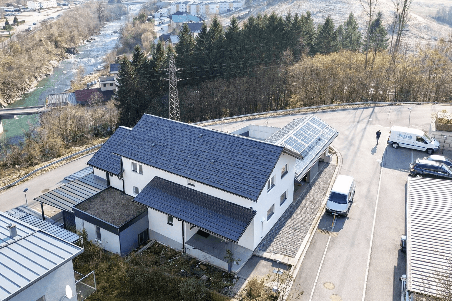 Luftaufnahme eines modernen Gebäudes mit Solaranlagen auf dem Dach und umliegender Landschaft.