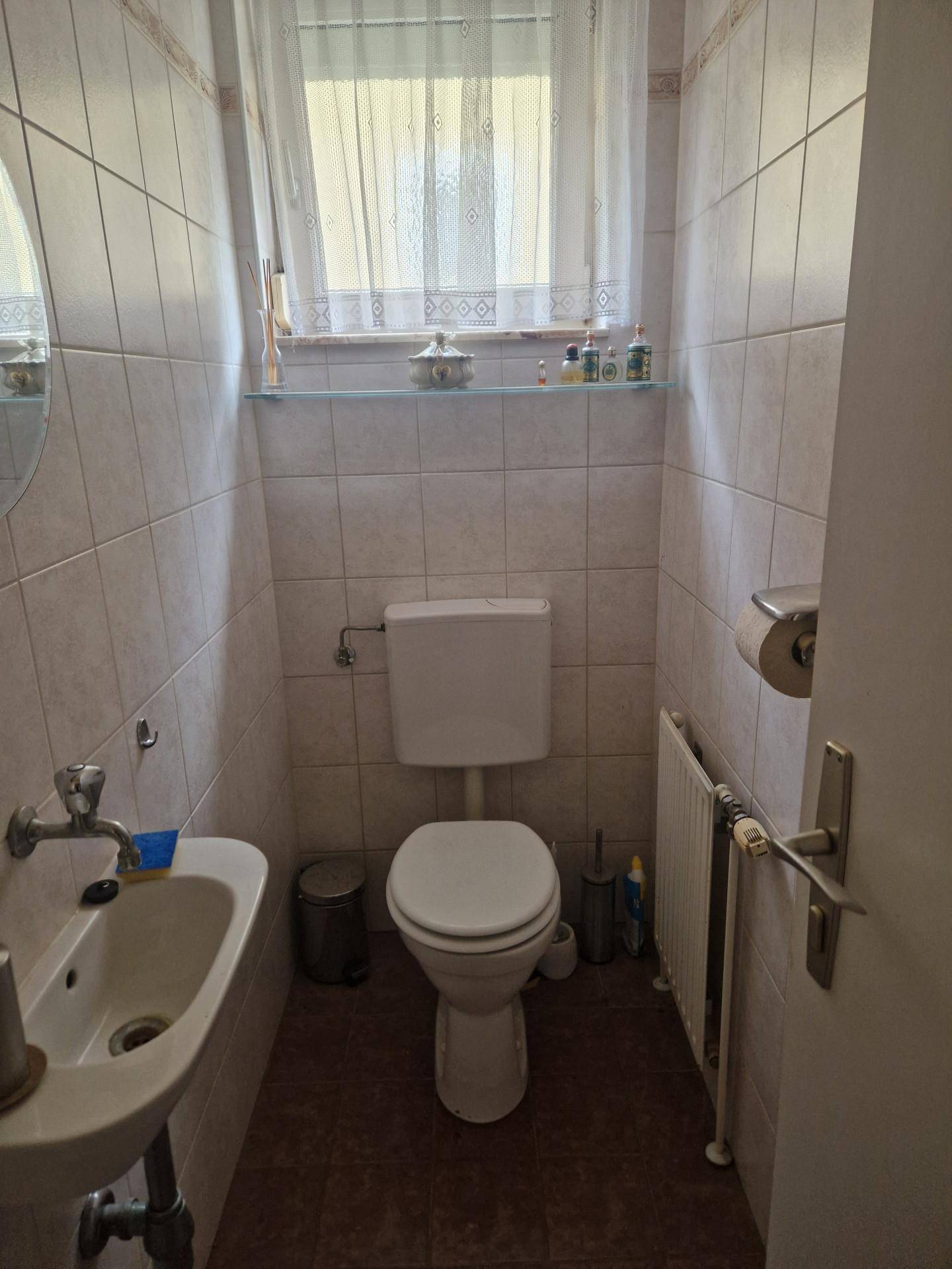 Separate Gästetoilette mit Waschbecken, WC und Fenster, hell gefliest und funktional.