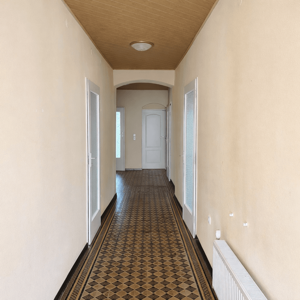Langer Flur mit gemusterten Bodenfliesen und einer Holzdecke, die Wärme ausstrahlt.