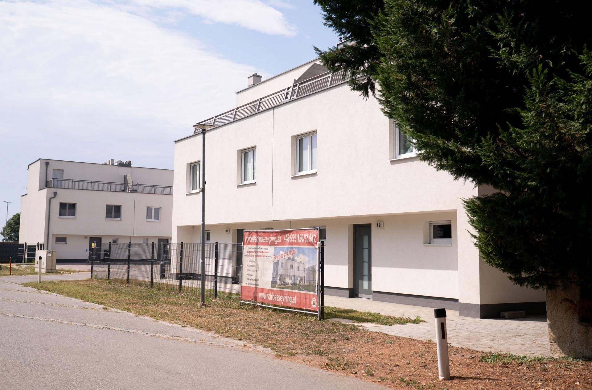 Moderne Reihenhäuser mit weißer Fassade und einem Verkaufsbanner im Vordergrund.