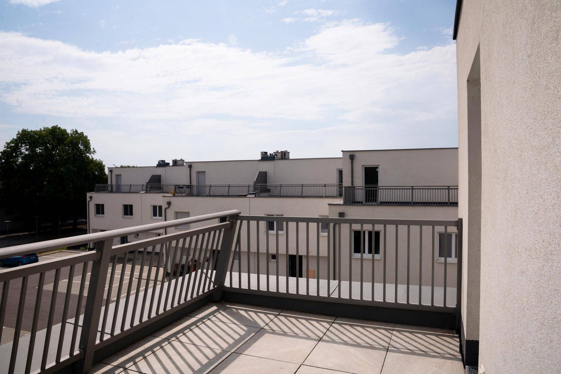 Geräumiger Balkon mit Fliesenboden und Blick auf die umliegenden Gebäude und den Hof.