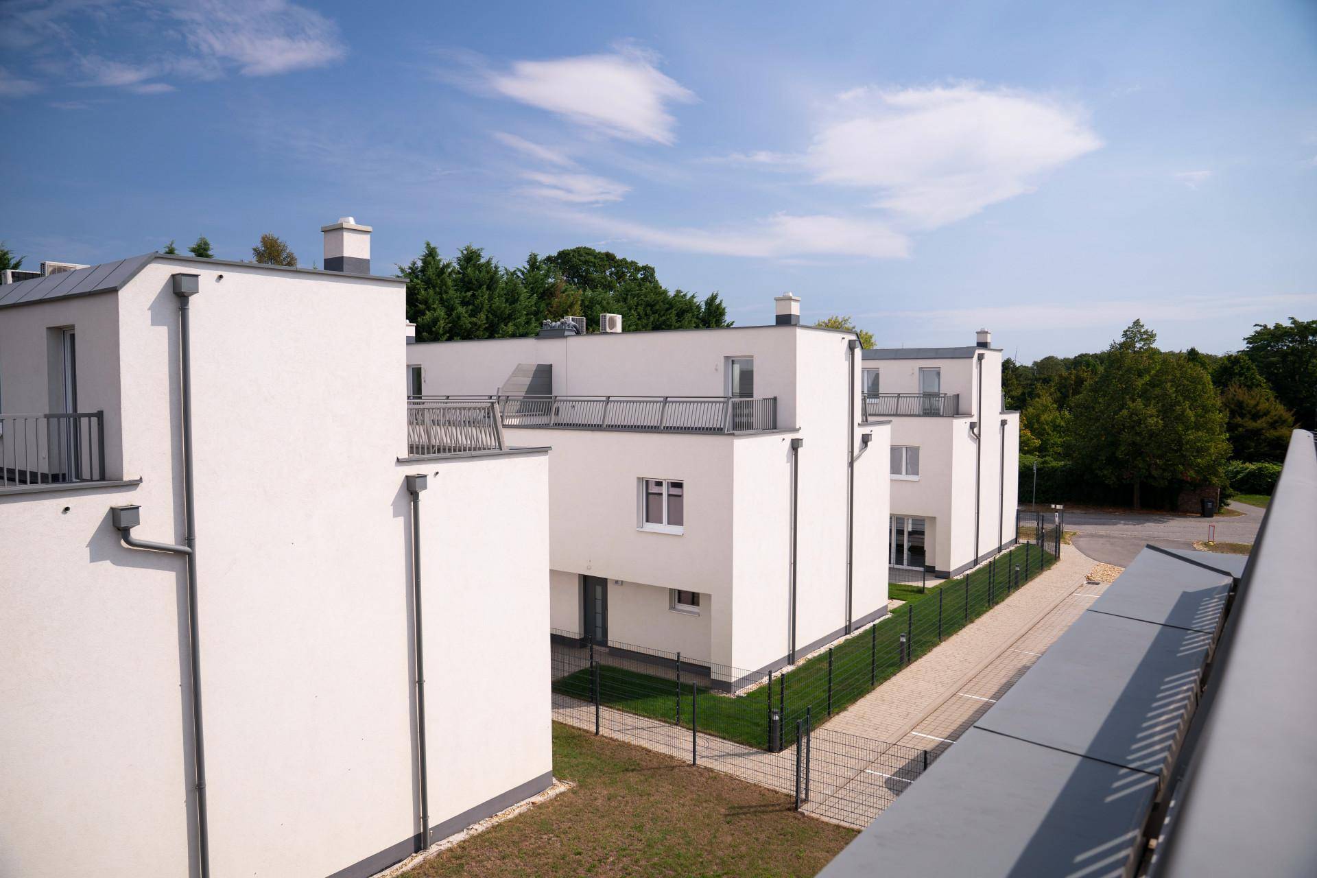 Reihe von modernen weißen Gebäuden mit Flachdächern und kleinen Balkonen unter blauem Himmel.