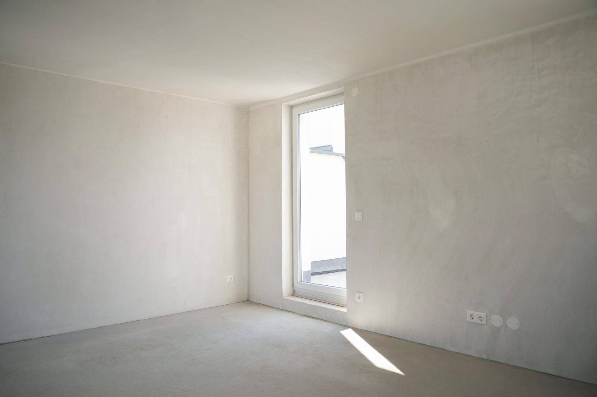 Heller, unmöblierter Raum mit großen Fenstern und Betonboden, bereit für den Ausbau.