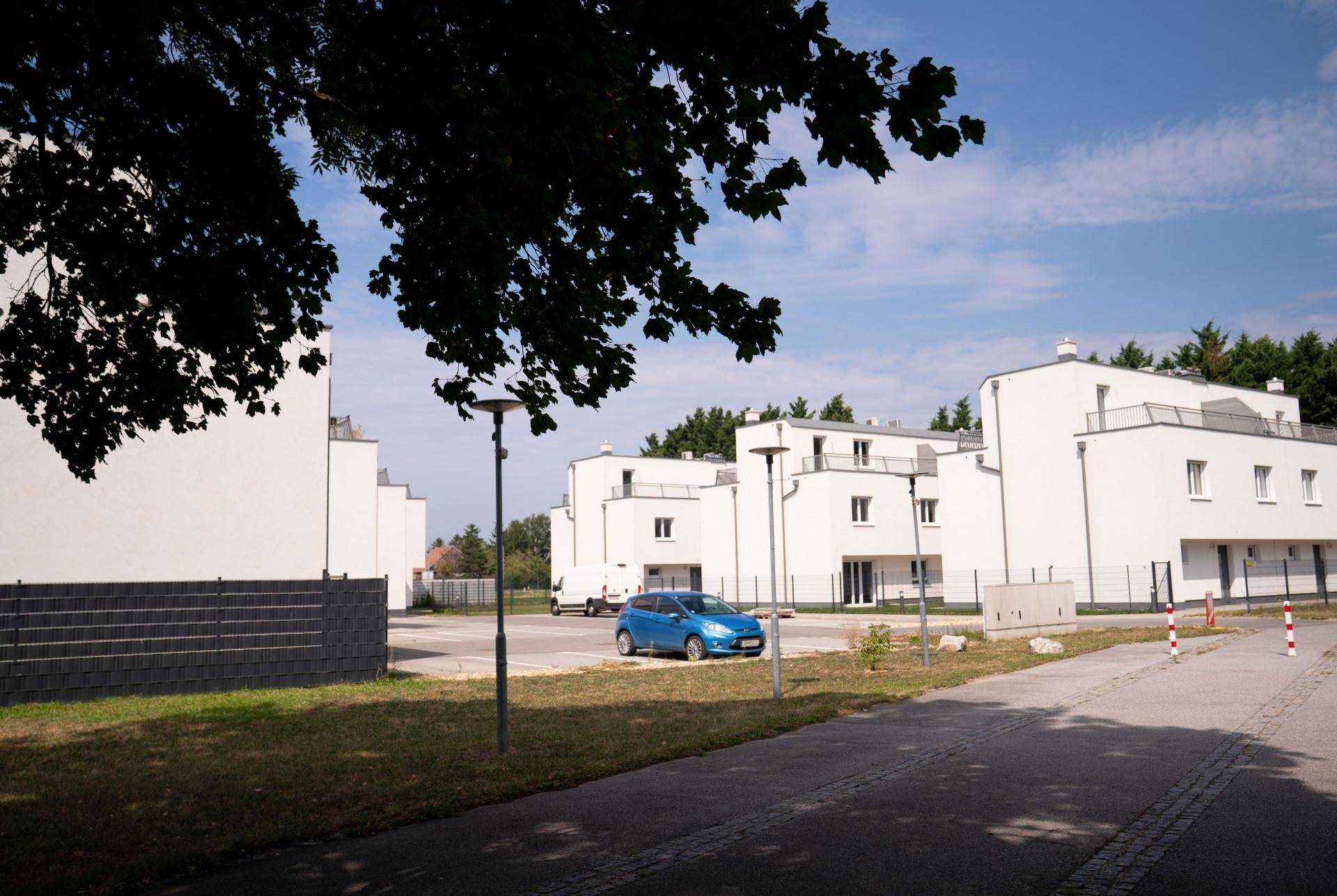 Mehrere moderne weiße Gebäude mit Flachdächern und einem Parkplatz unter blauem Himmel.