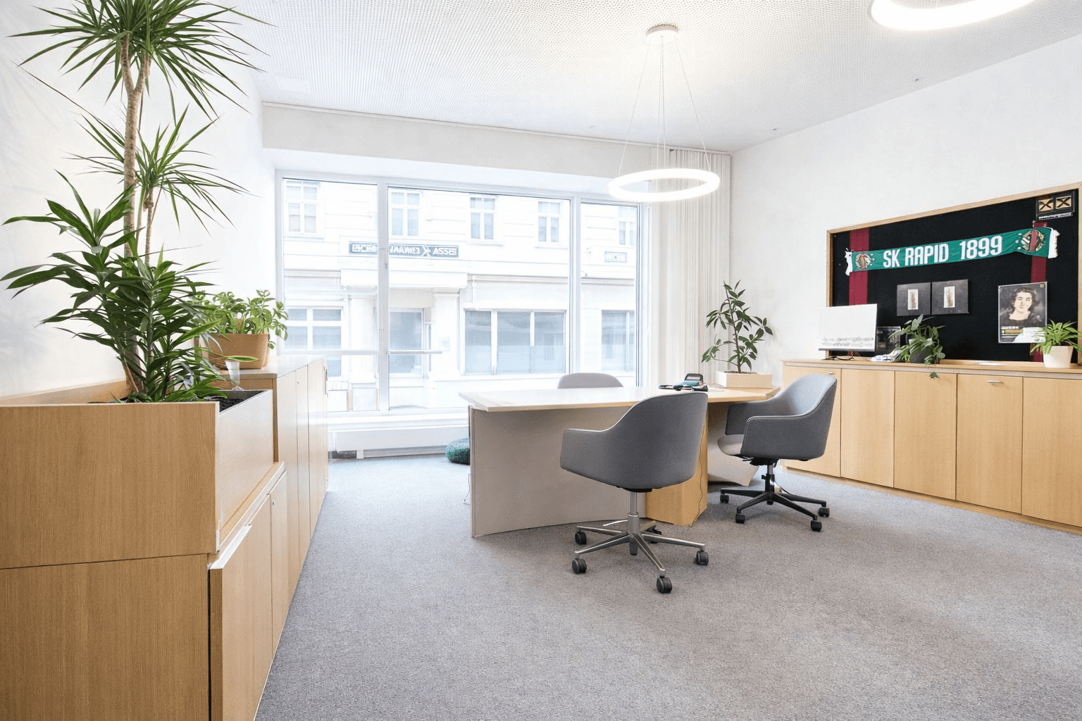 Modernes Büro mit viel Tageslicht, Pflanzen und Holzmöbeln, bietet eine angenehme Arbeitsatmosphäre.