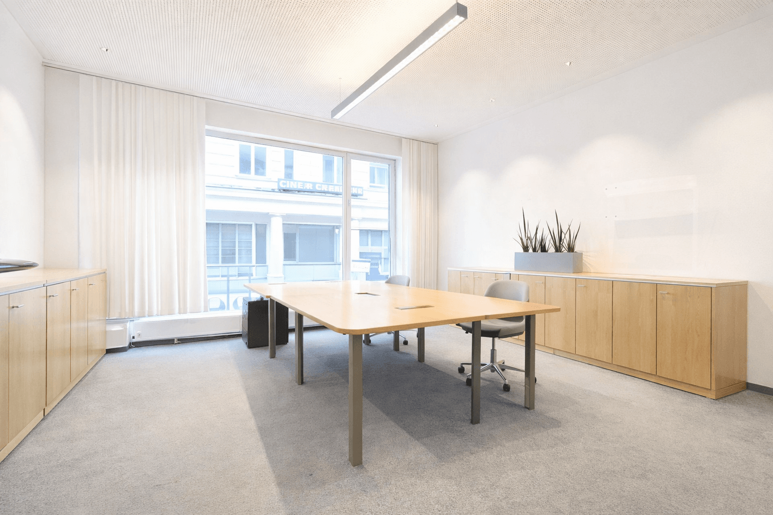 Geräumiger Besprechungsraum mit hellem Holztisch, Teppichboden und großen Fenstern für viel Tageslicht.