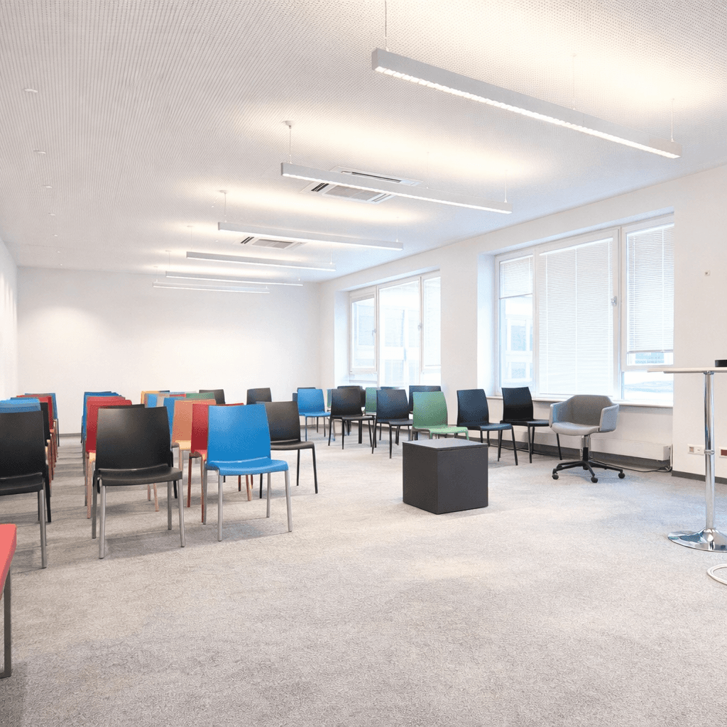 Großer Konferenzraum mit Reihen bunter Stühle, Teppichboden und hellen Wänden, bereit für Präsentationen.