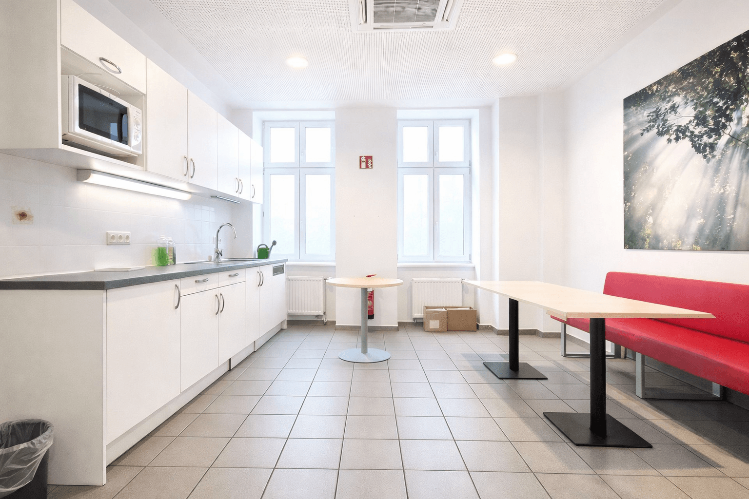 Funktionale Küche mit weißen Schränken, Fliesenboden und Essbereich, ausgestattet mit Mikrowelle und Spüle.