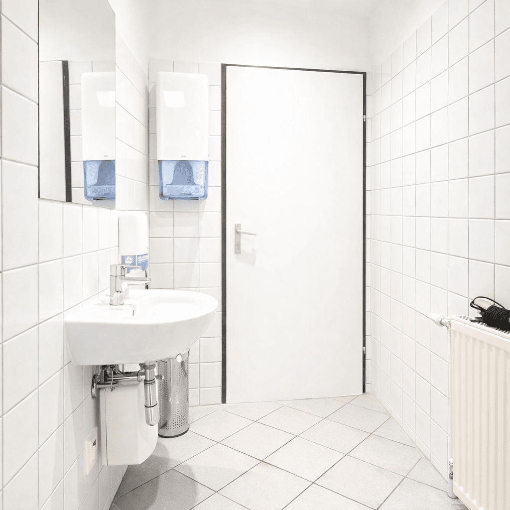 Sauberes Badezimmer mit weißen Fliesen, Waschbecken und Spender für Seife und Papierhandtücher.