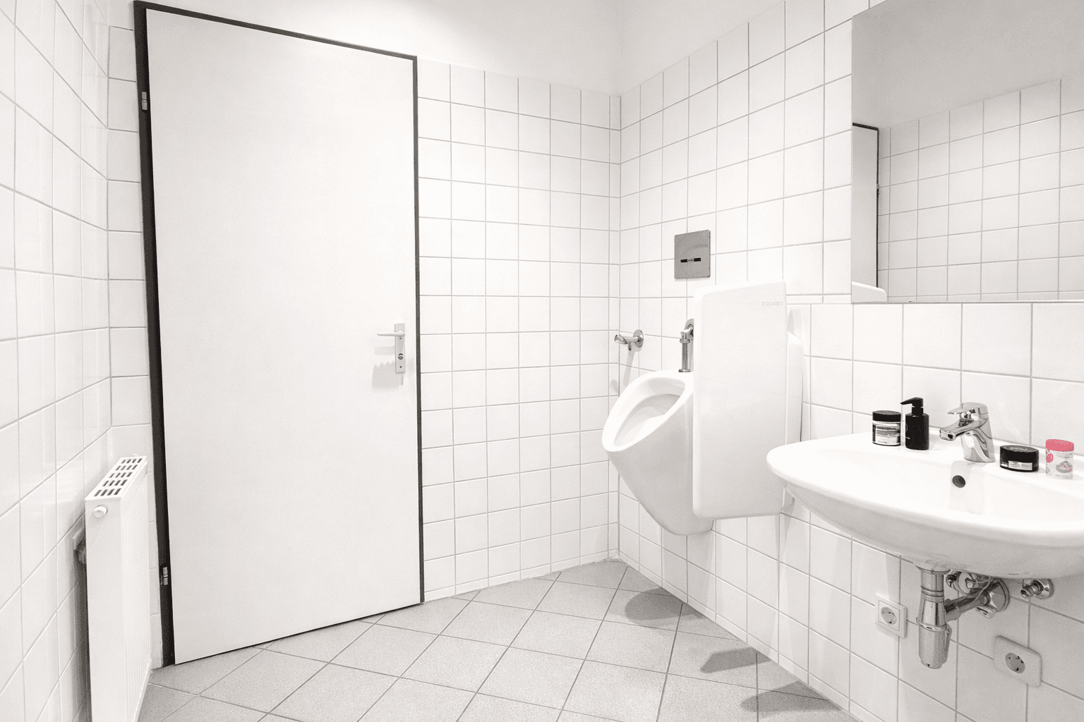 Modernes Badezimmer mit weißen Fliesen, Urinal und Waschbecken, sehr sauber und funktional gestaltet.