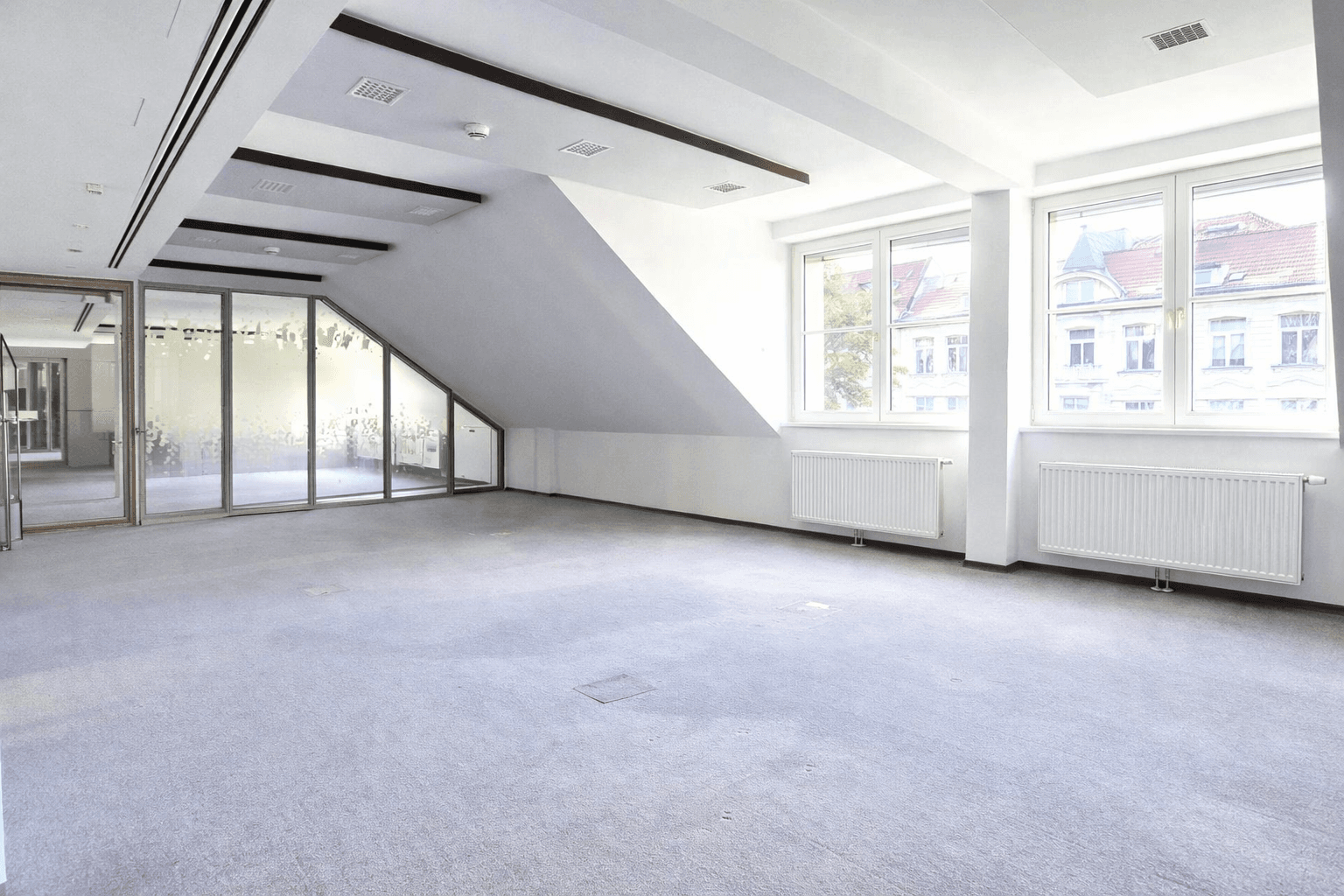 Großes, helles Büro mit Teppichboden, mehreren Fenstern und schrägen Deckenbereichen.