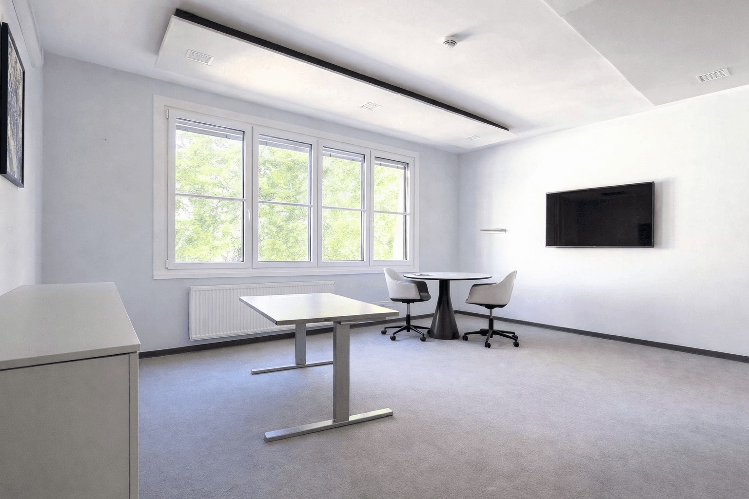 Modernes Büro oder Besprechungsraum mit Teppichboden, großen Fenstern und Wandfernseher.