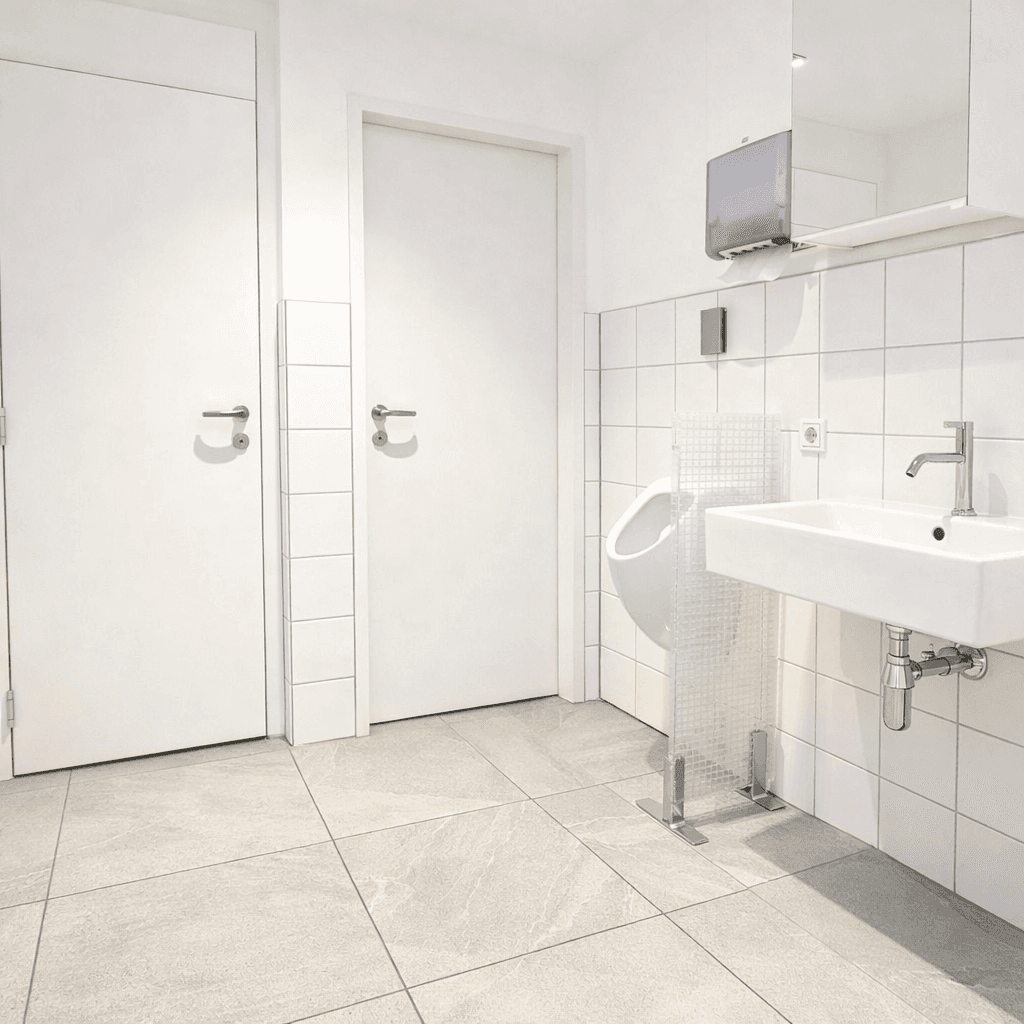 Sauberes Badezimmer mit weißen Fliesen, Waschbecken, Urinal und zwei Toilettenkabinen.