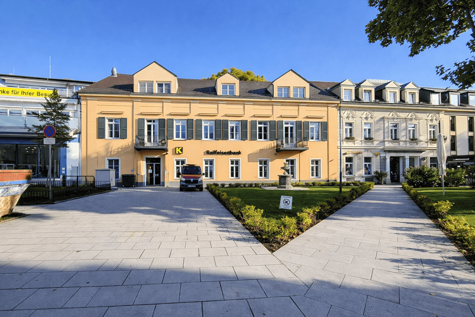 Historisches Gebäude mit gelber Fassade, grünen Fensterläden und einem gepflegten Vorgarten.