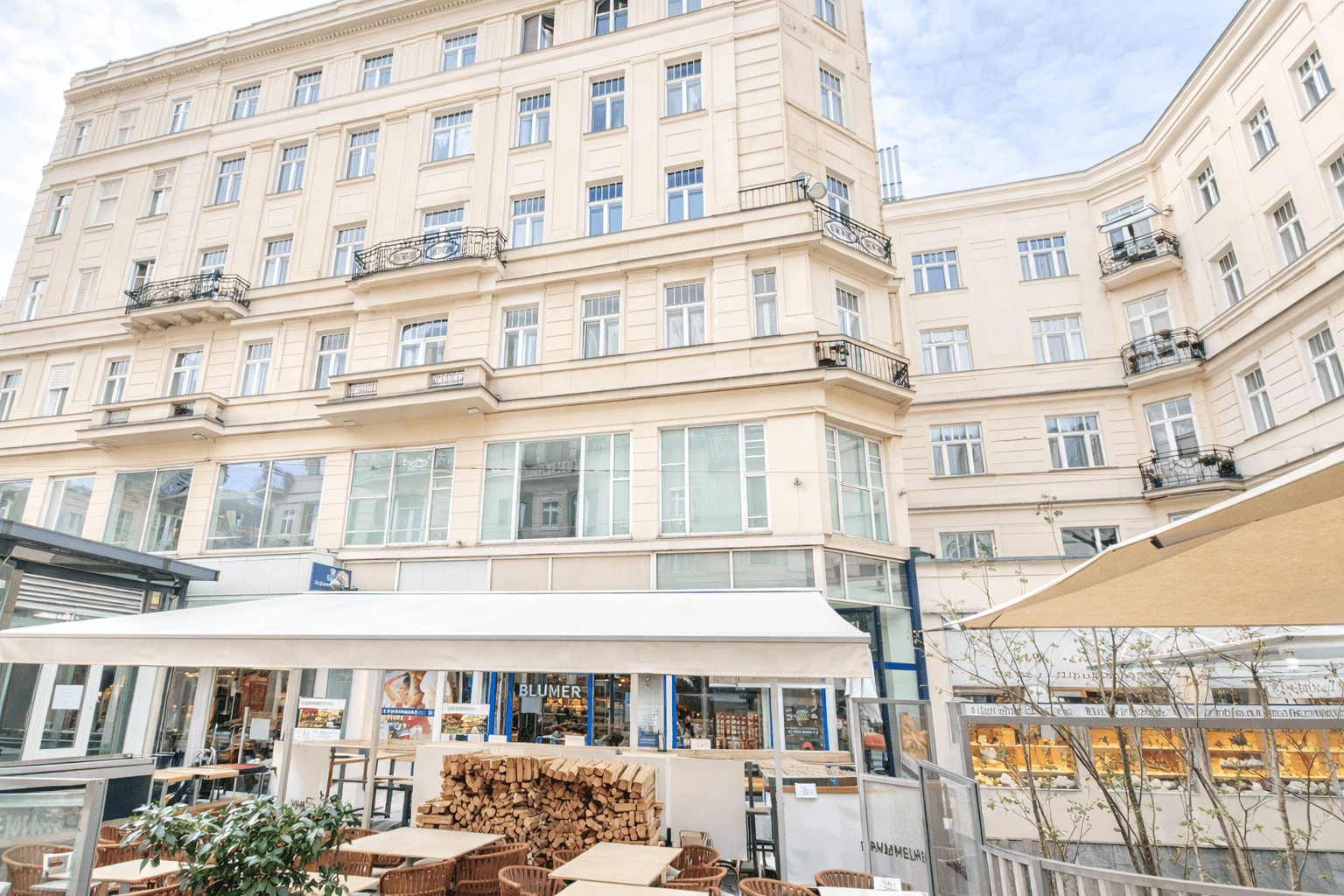 Historisches Gebäude mit klassischer Fassade, vielen Fenstern und Balkonen, belebt durch Straßencafés.