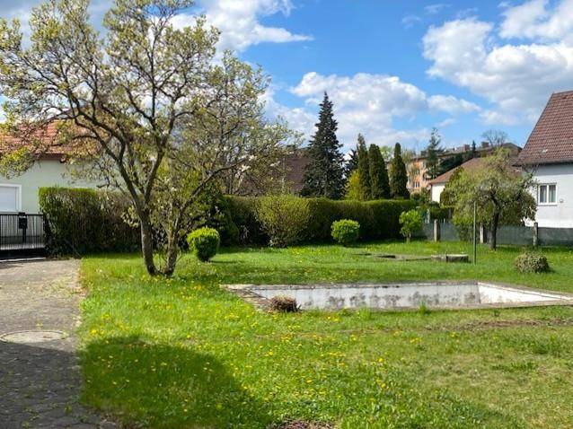 Großer Gartenbereich mit Rasenfläche, Hecken, Bäumen und einem unfertigen Pool.