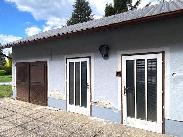 Außenansicht eines Nebengebäudes oder einer Garage mit mehreren Türen und gepflastertem Vorplatz.
