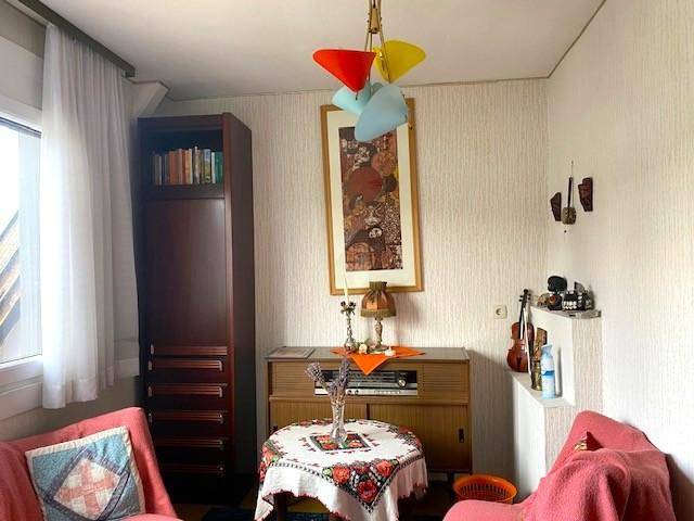 Wohn- oder Arbeitszimmer mit kleinem Rundtisch, Sessel und verschiedenen Dekorationsgegenständen.