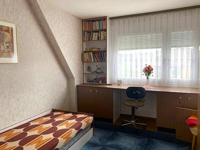 Schlaf- oder Arbeitszimmer mit Einzelbett, Schreibtisch, Bücherregalen und einem Fenster.