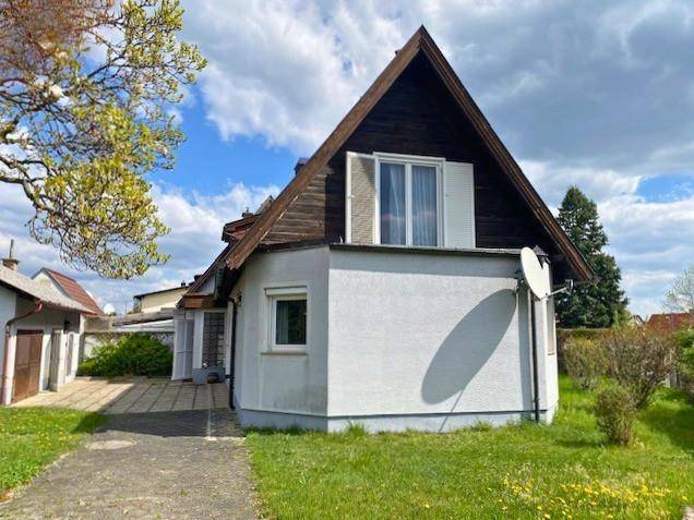 Seitenansicht des Hauses mit markantem Giebel, Satellitenschüssel und gepflasterter Auffahrt.