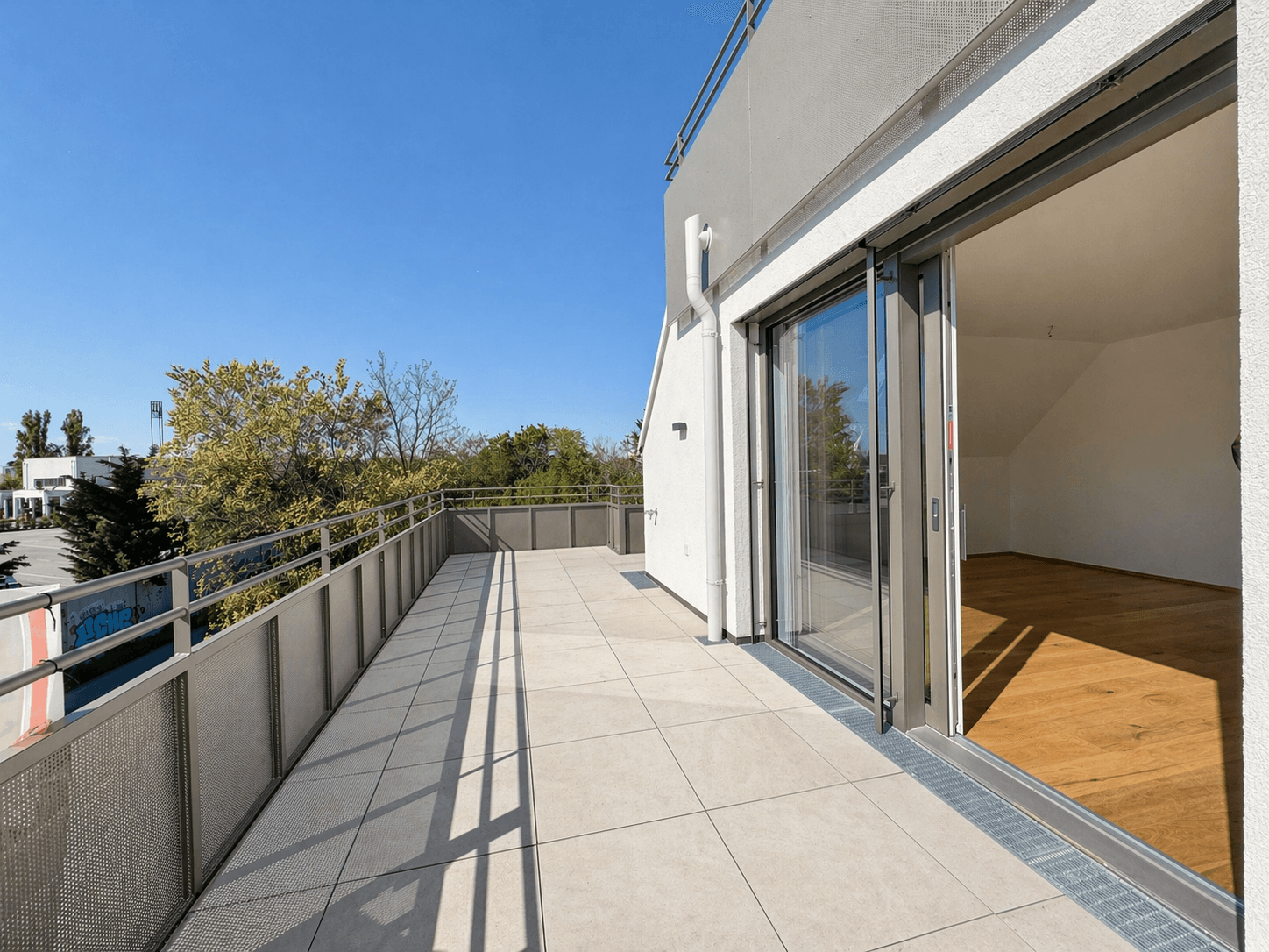 Großzügige Dachterrasse mit Fliesenboden und weitem Blick unter strahlend blauem Himmel.
