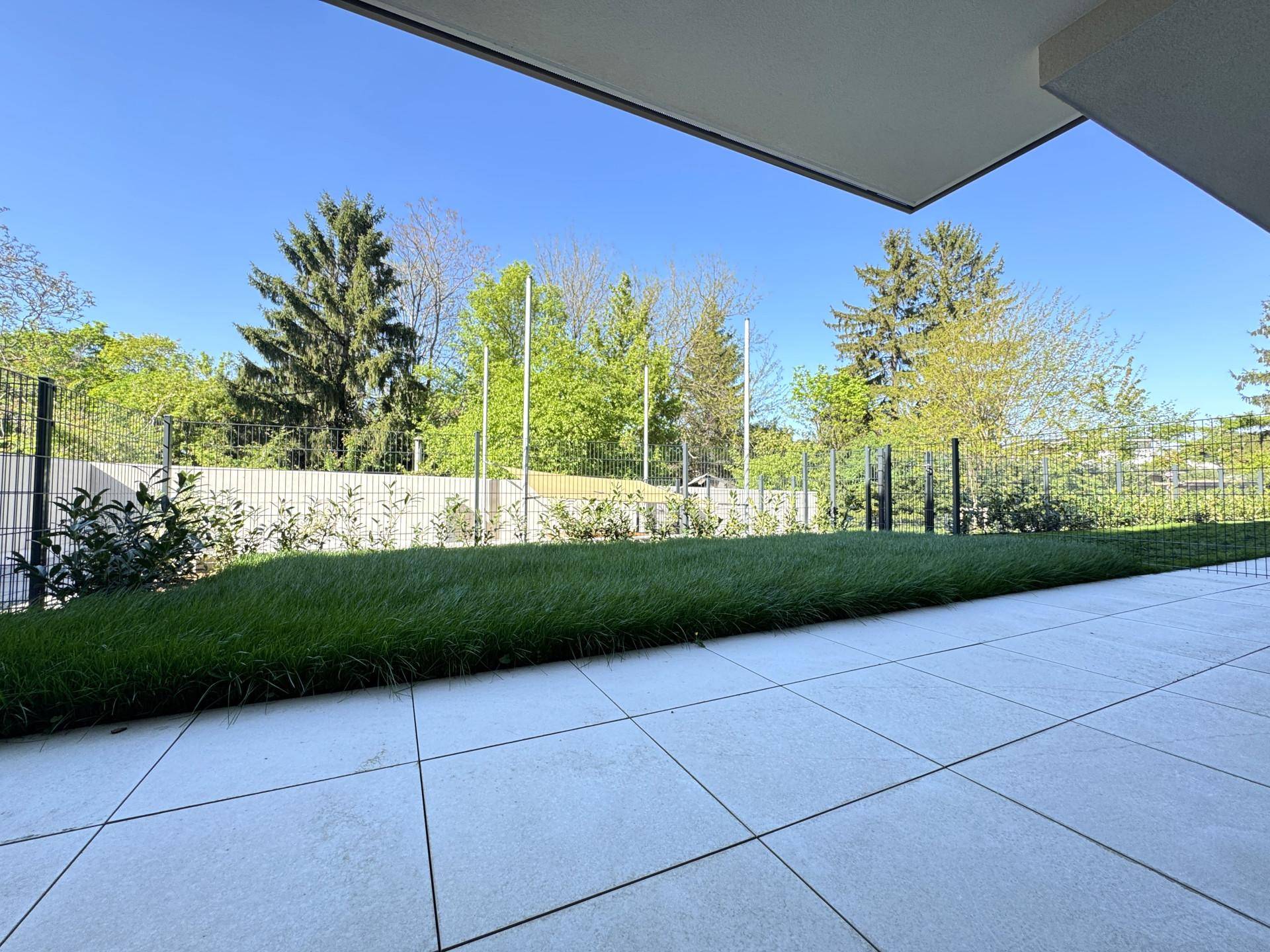 Gepflegte Gartenfläche im Erdgeschoss mit gefliester Terrasse und Rasenbereich, umgeben von Bäumen.