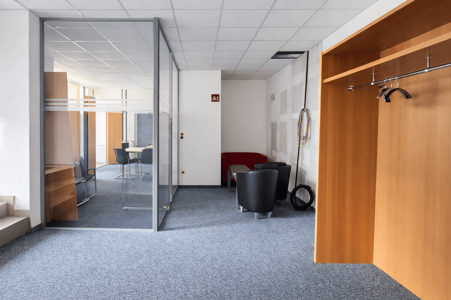 Flurbereich mit Glaswänden zu einem Konferenzraum, Teppichboden und Garderobe.
