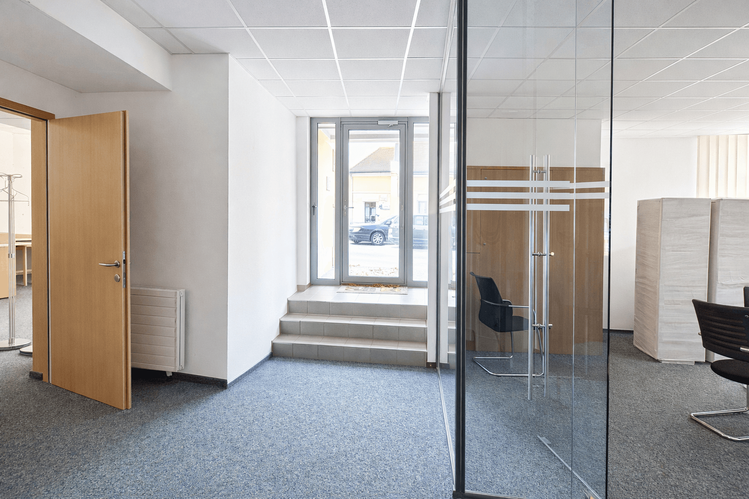 Eingangsbereich mit Glastür zur Straße, Treppe und Zugang zu Büroräumen.